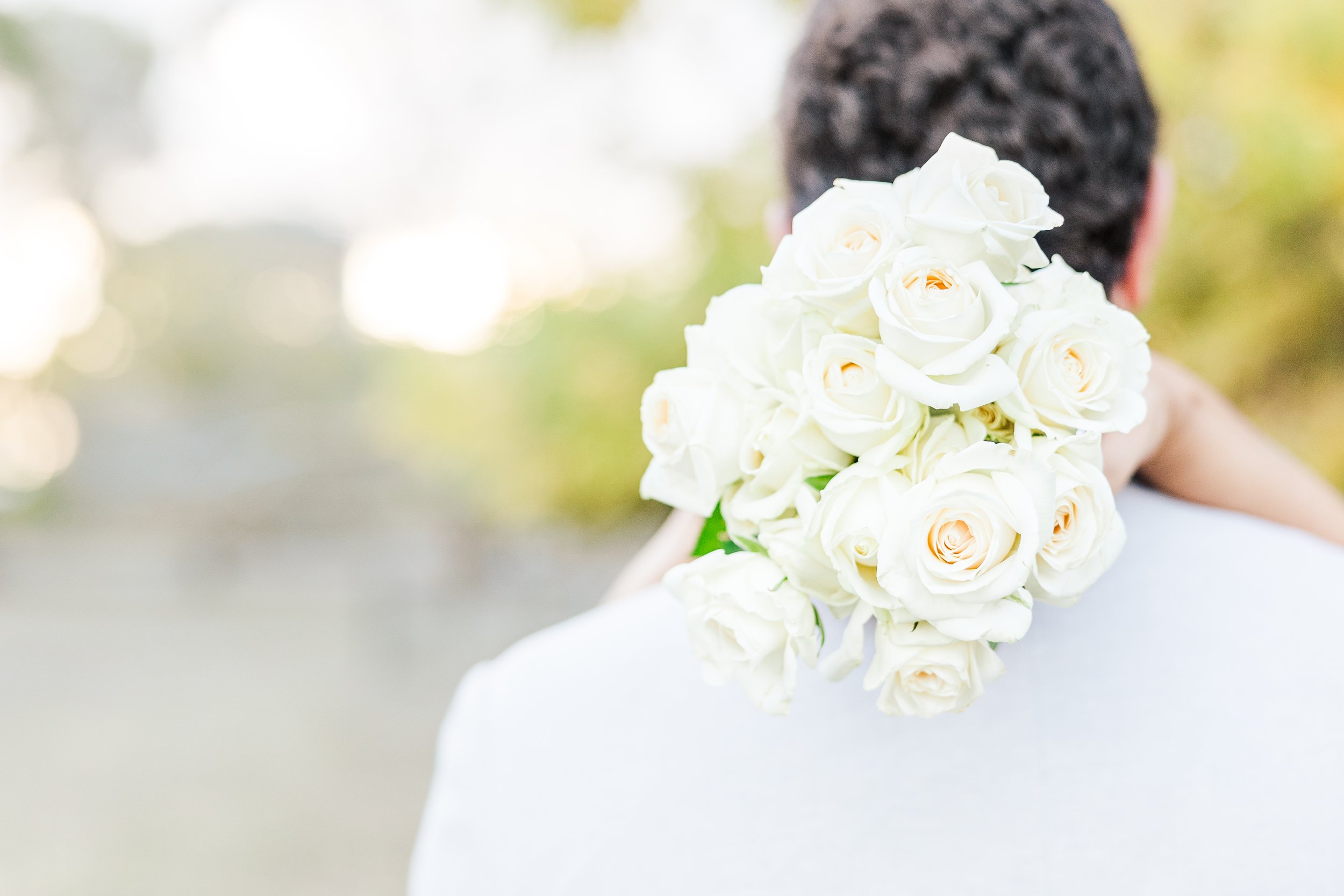 Person holding a bouquet of white roses over their shoulder during an outdoor event.