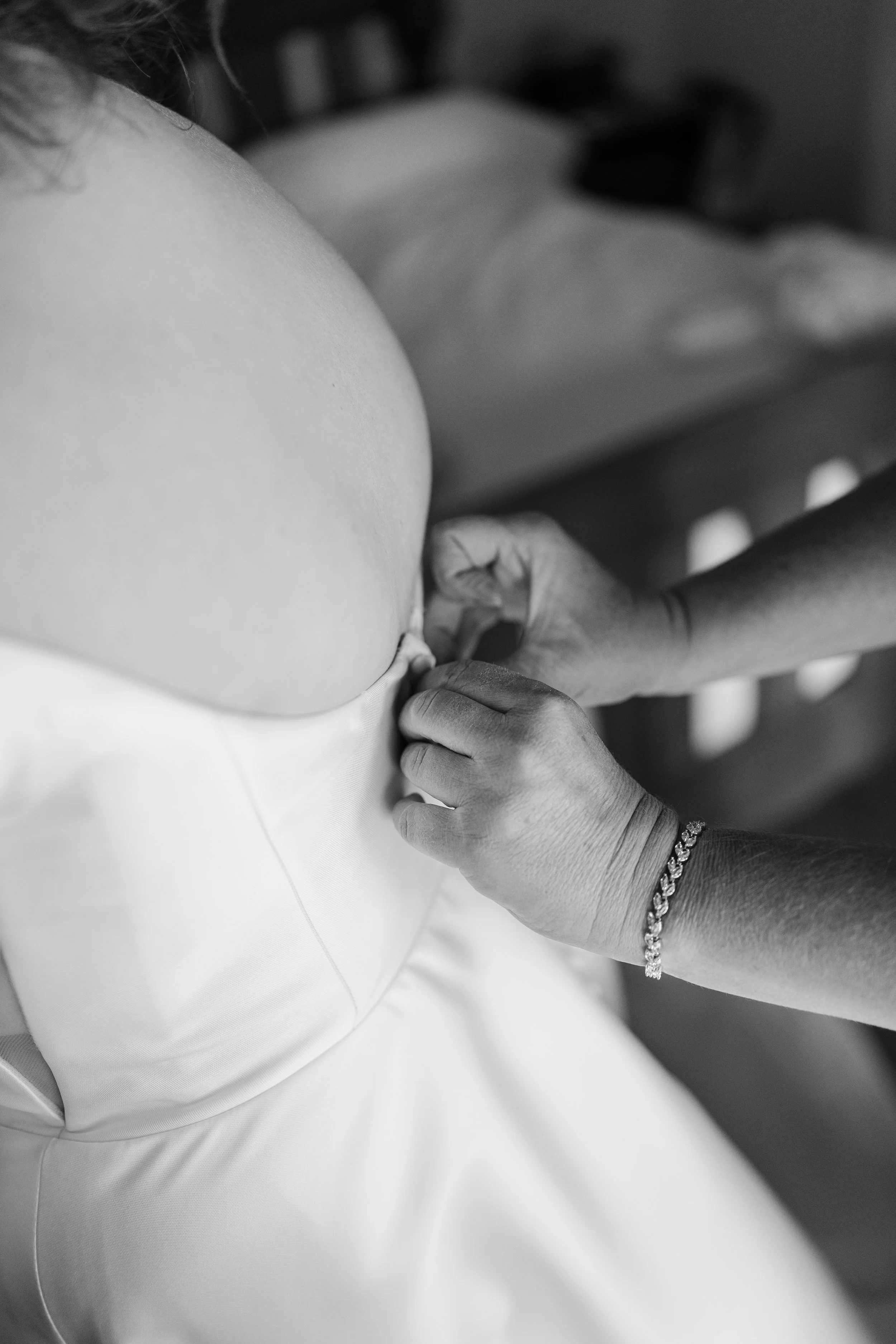 A person is buttoning up the back of a wedding dress with another person helping.