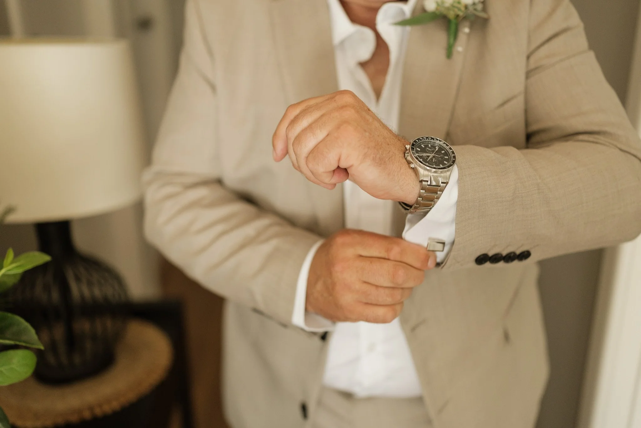 Person wearing a beige suit with a watch adjusting their cuff in an indoor setting.