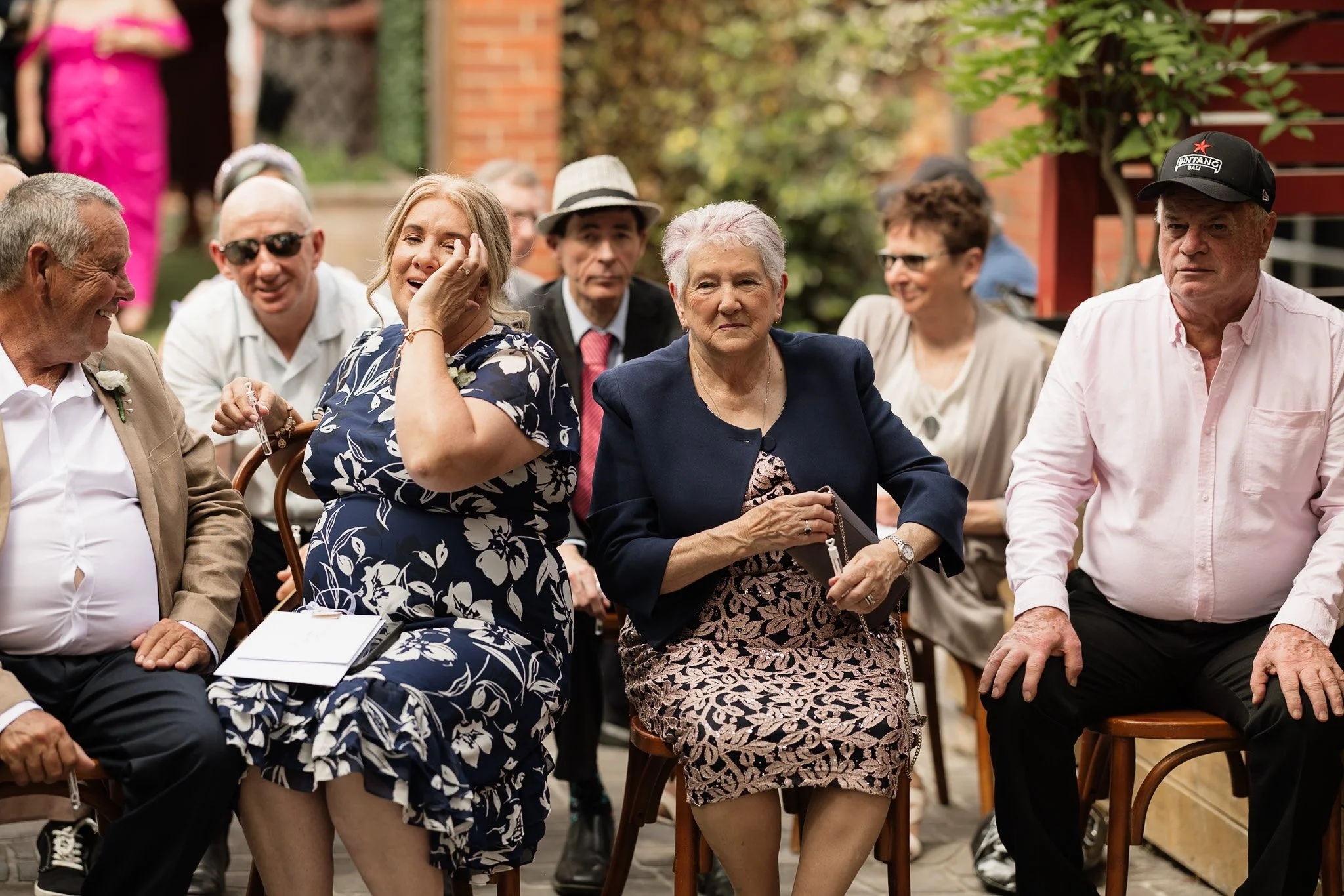 A group of people sitting outdoors, some smiling and laughing, during a social gathering or event.