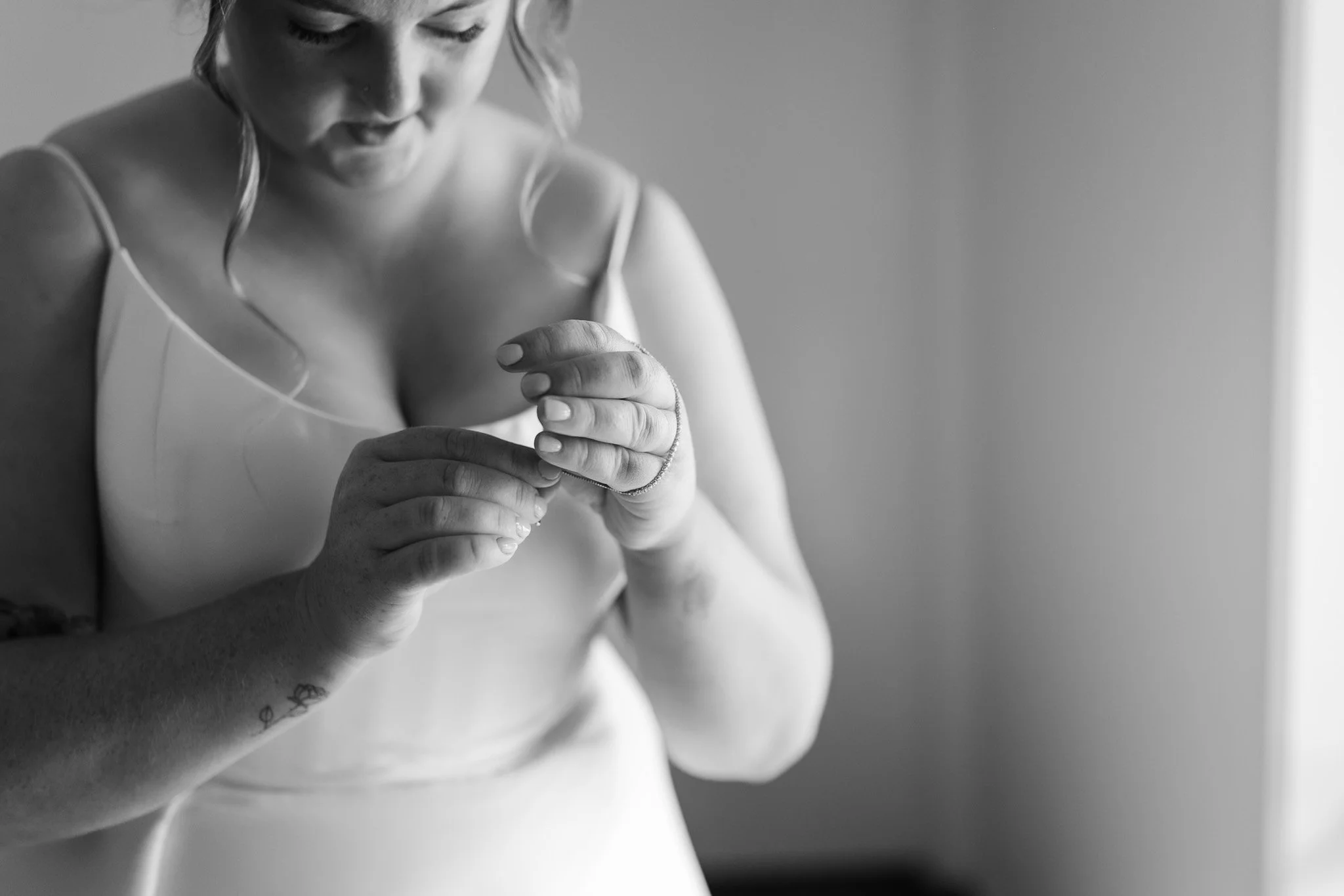 Black and white photo of a woman wearing a tank top, looking down and examining her hand, with a slight smile.