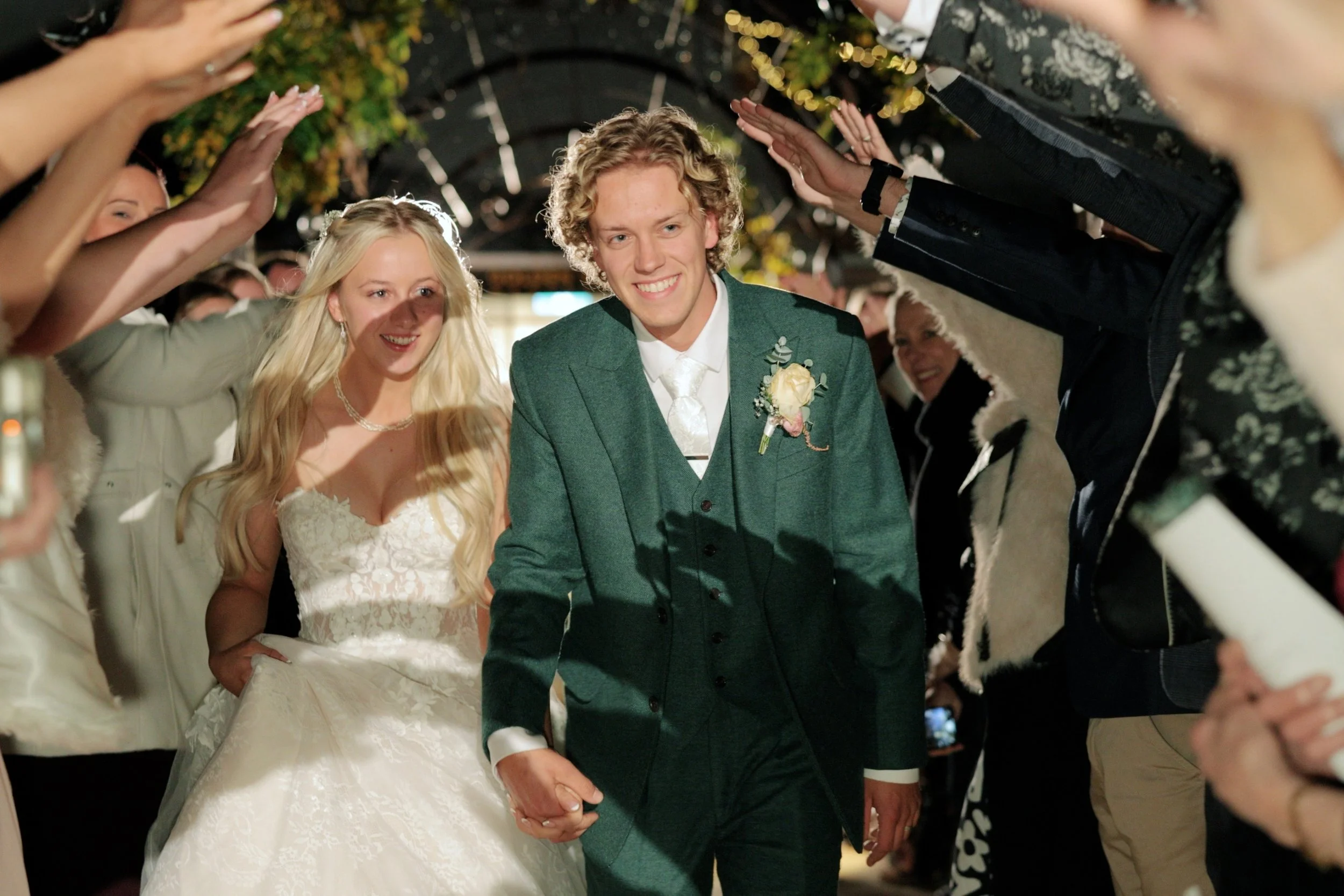 A bride and groom walking hand in hand through a tunnel of friends or family members at their wedding reception.
