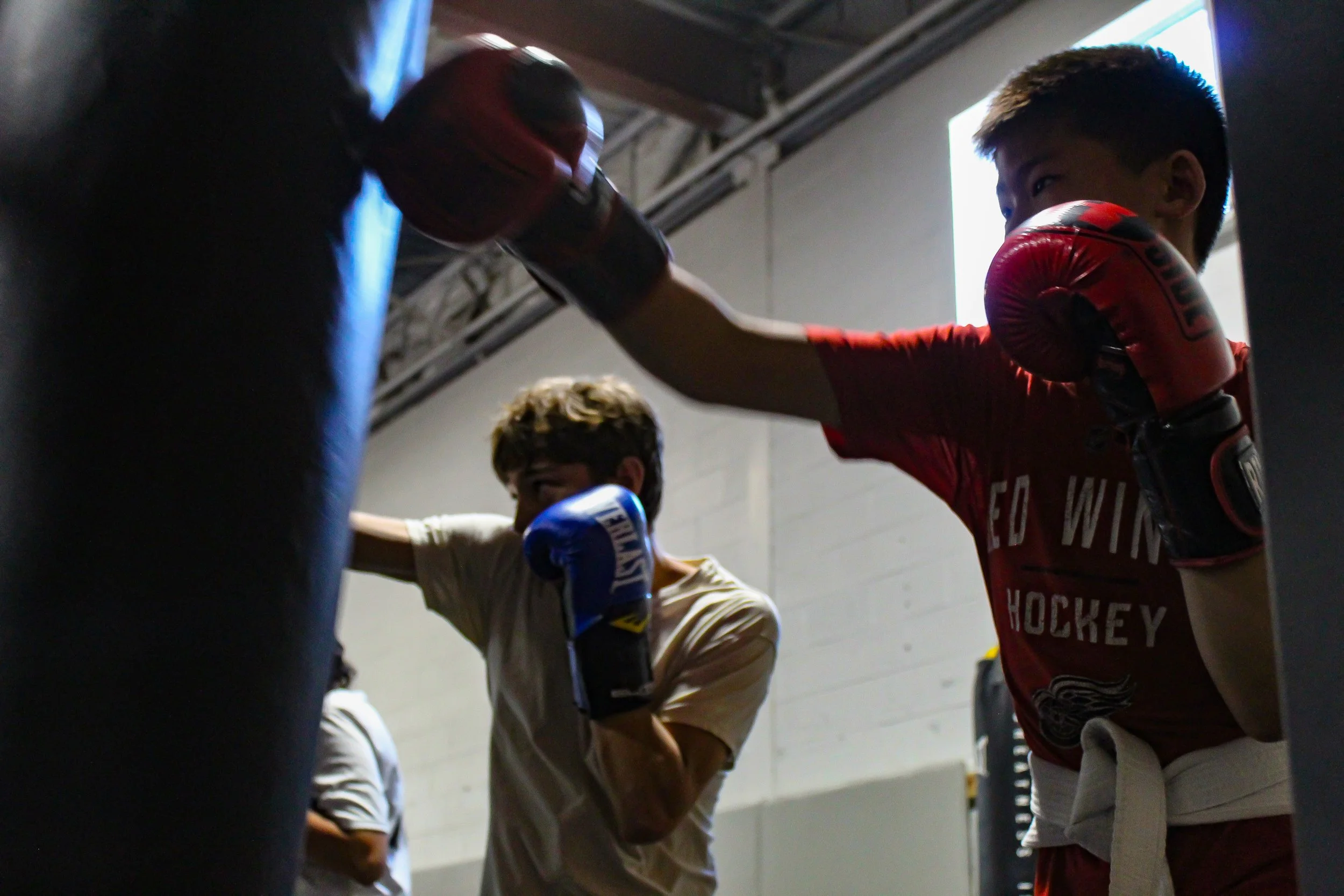 Two young boys boxing and practicing punches on a heavy bag in a gym.