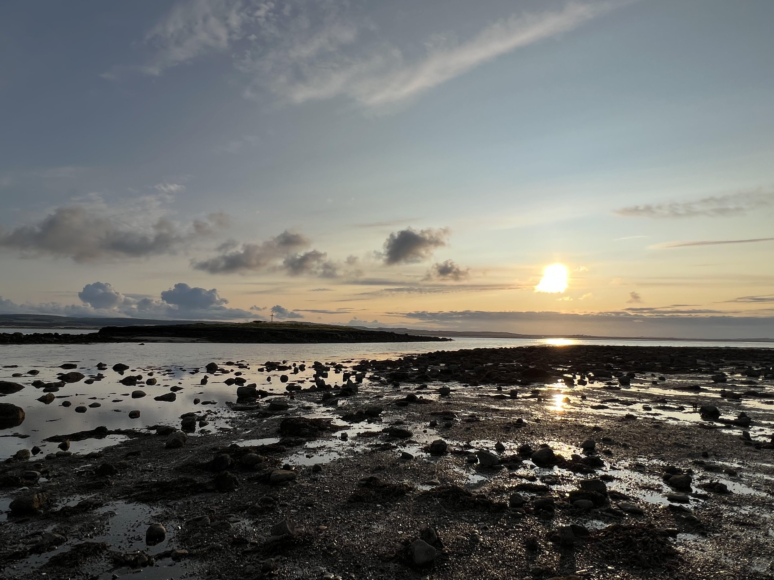 A rocky beach at sunrise, looking out towards an expansive bay