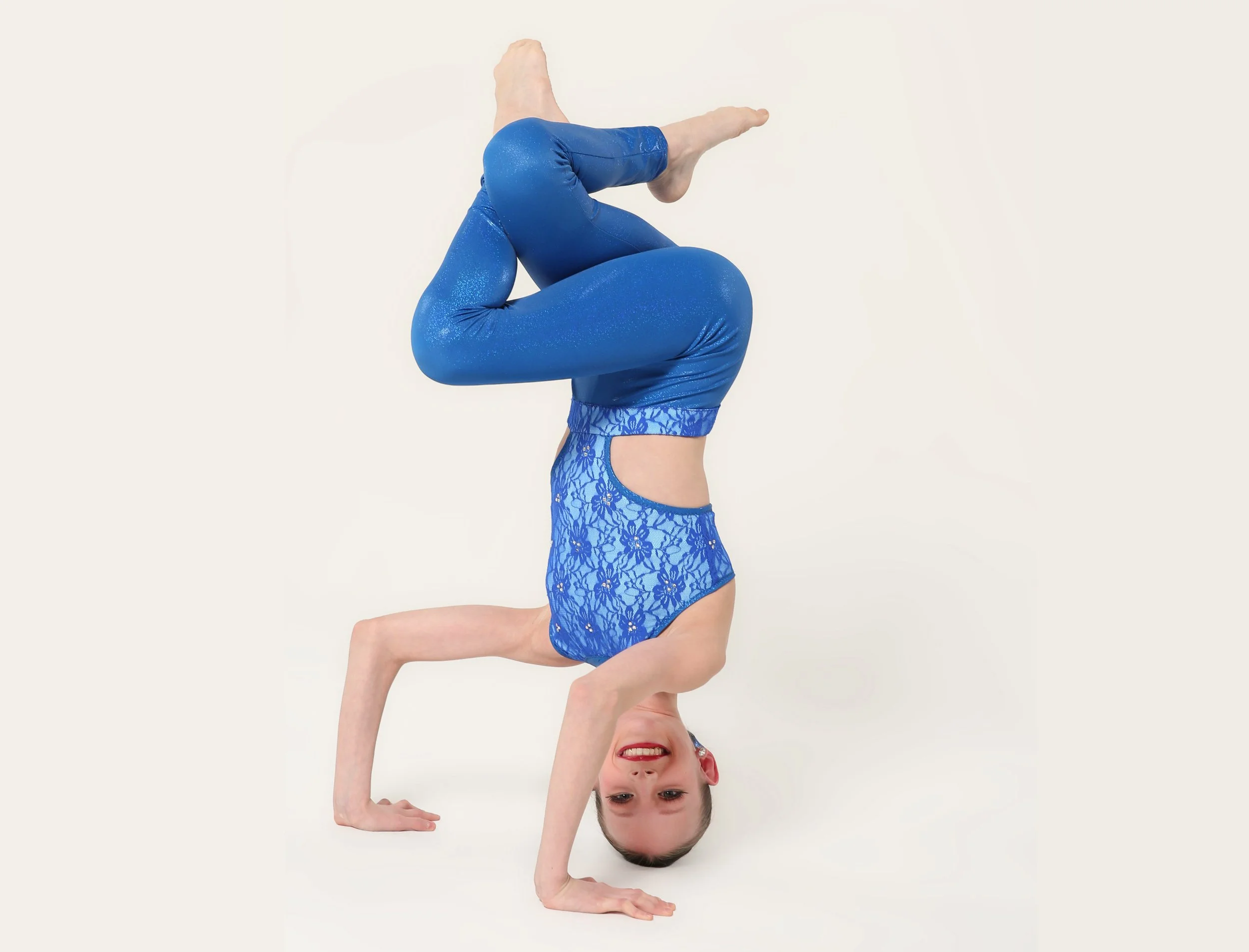 A woman performing a handstand in a maroon, studded, semi-transparent dance costume against a plain white background.