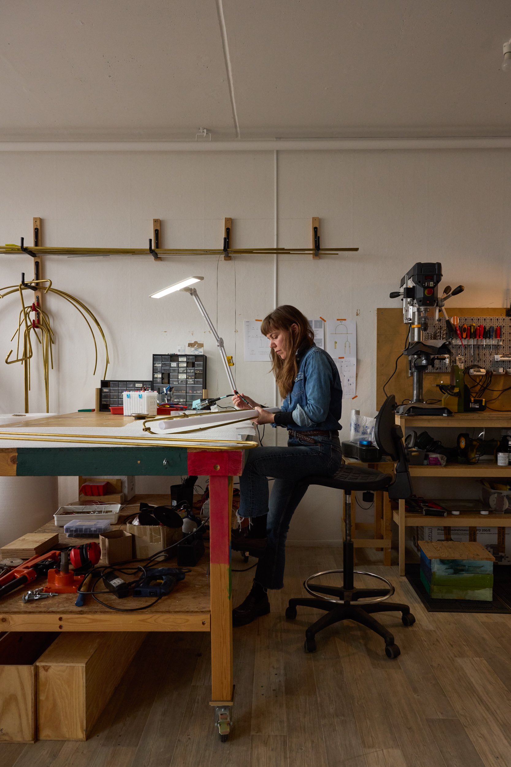 Woman working at a cluttered workbench with tools and materials, in a workshop or maker space.