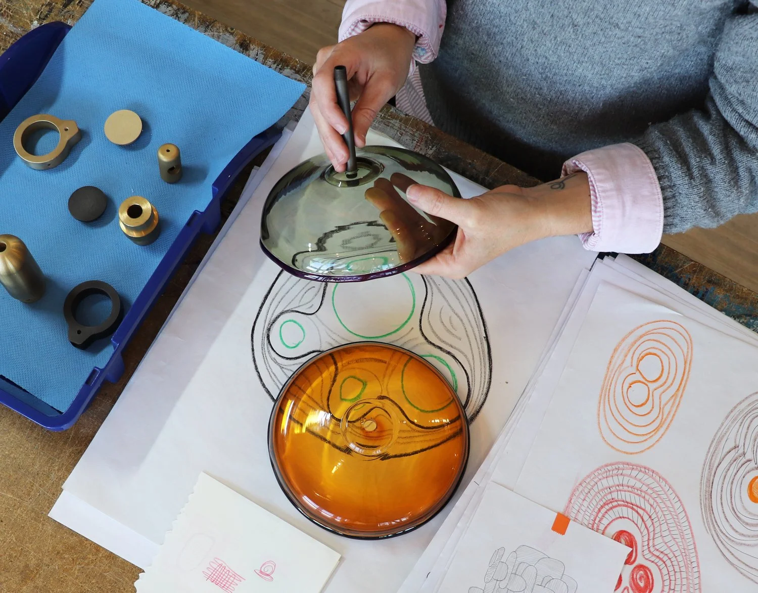 A person working with colorful glass pieces and sketches, making a fused glass art piece.