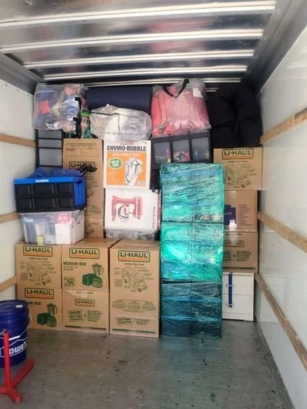 Packed moving truck with boxes labeled U-Haul, plastic storage bins, and household items.