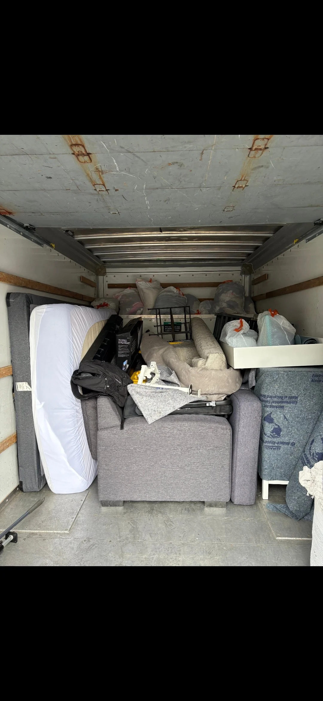 a garage filled with various household items, including a gray sofa, a mattress, bags of items, and miscellaneous furniture and boxes