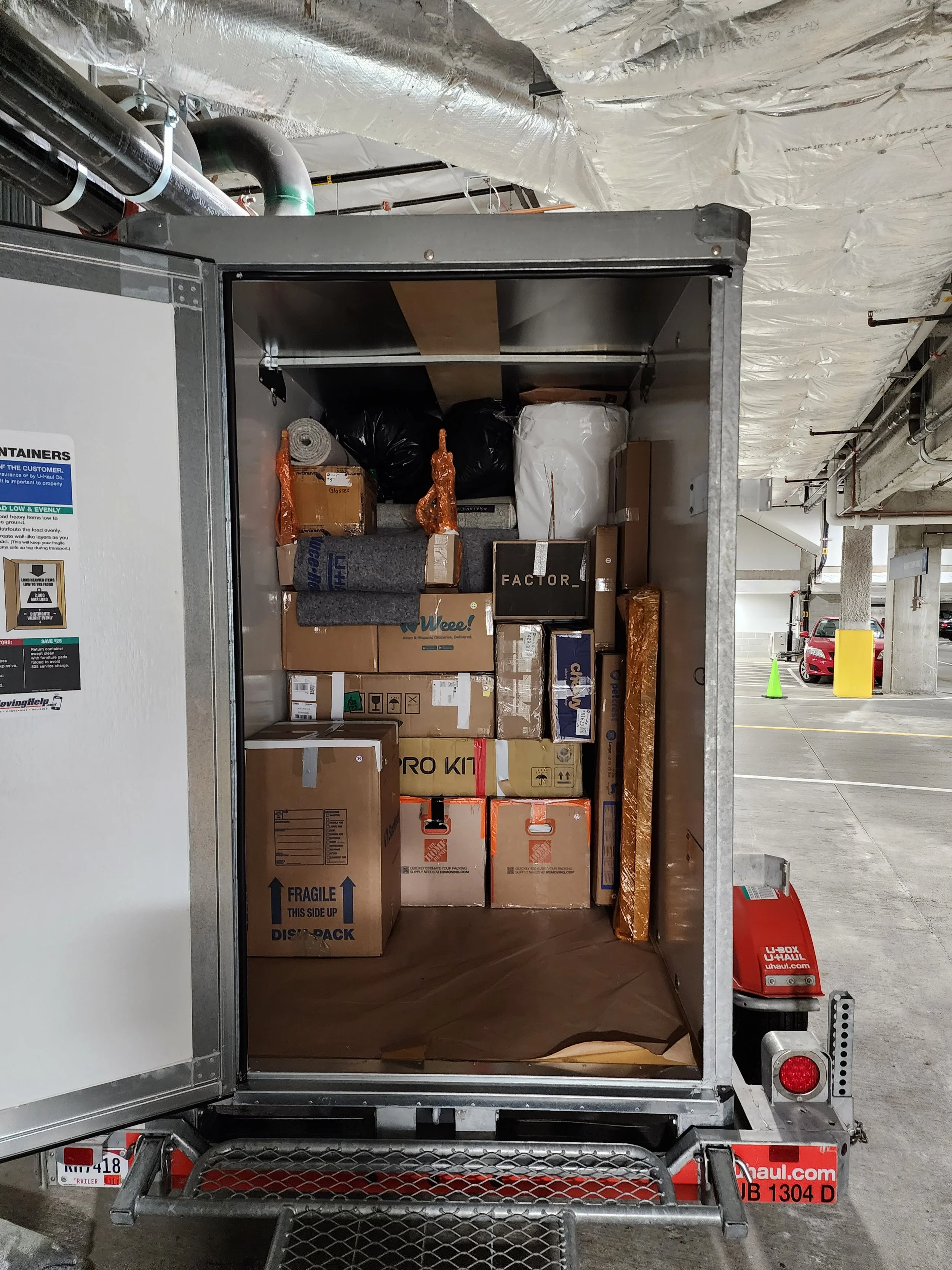 Back of a U-Haul truck filled with various boxes, and packing materials, parked in a parking garage.