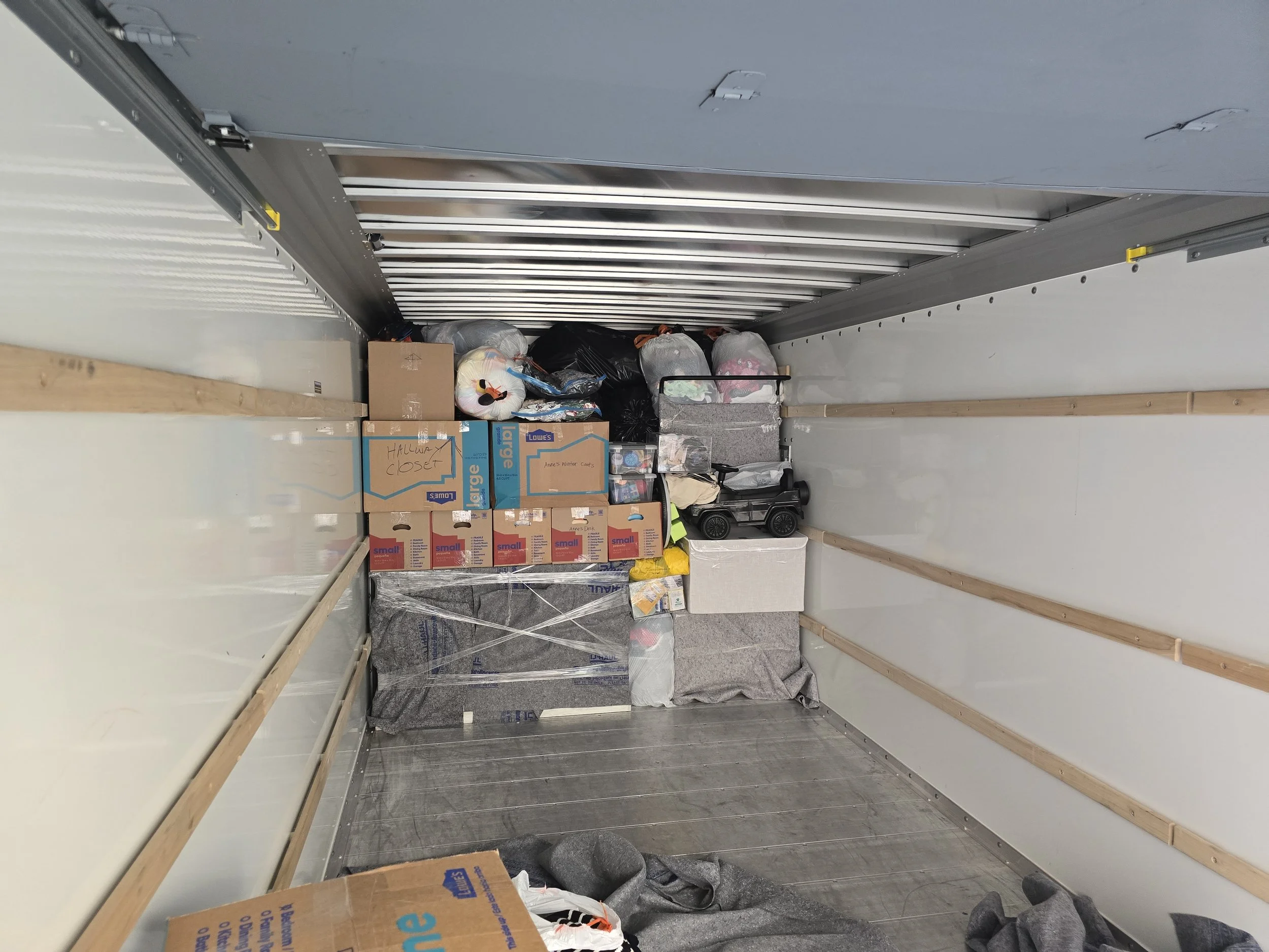 Empty moving truck with packed boxes and bags against the back wall.