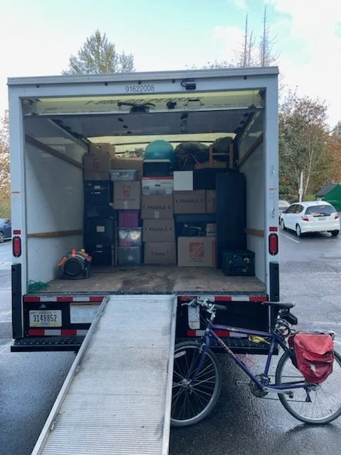 Open moving truck with boxes and items inside, a bicycle with a red bag attached parked in front.