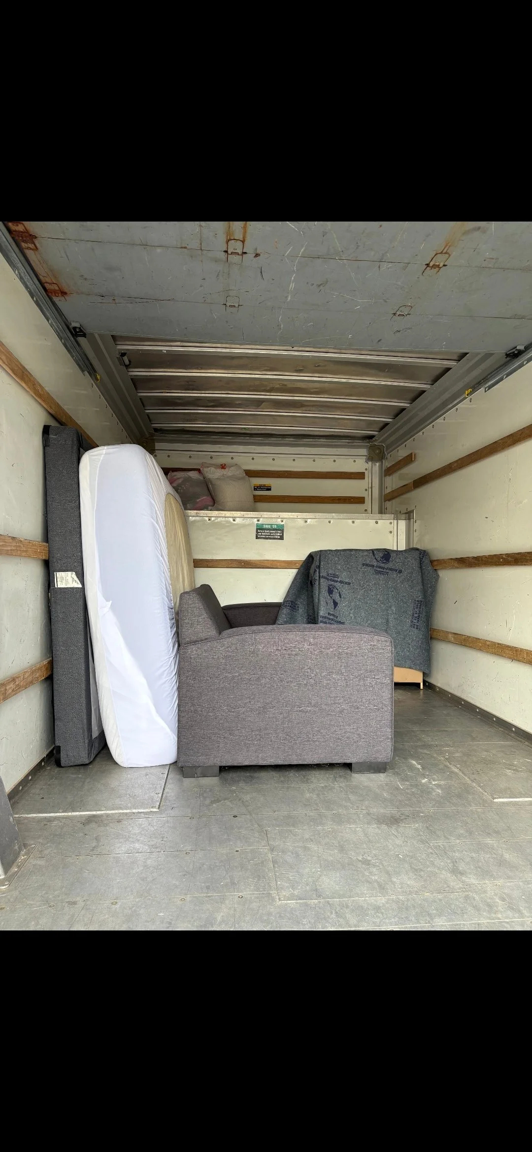 Interior of a moving truck with furniture, a mattress, and boxes stored inside.