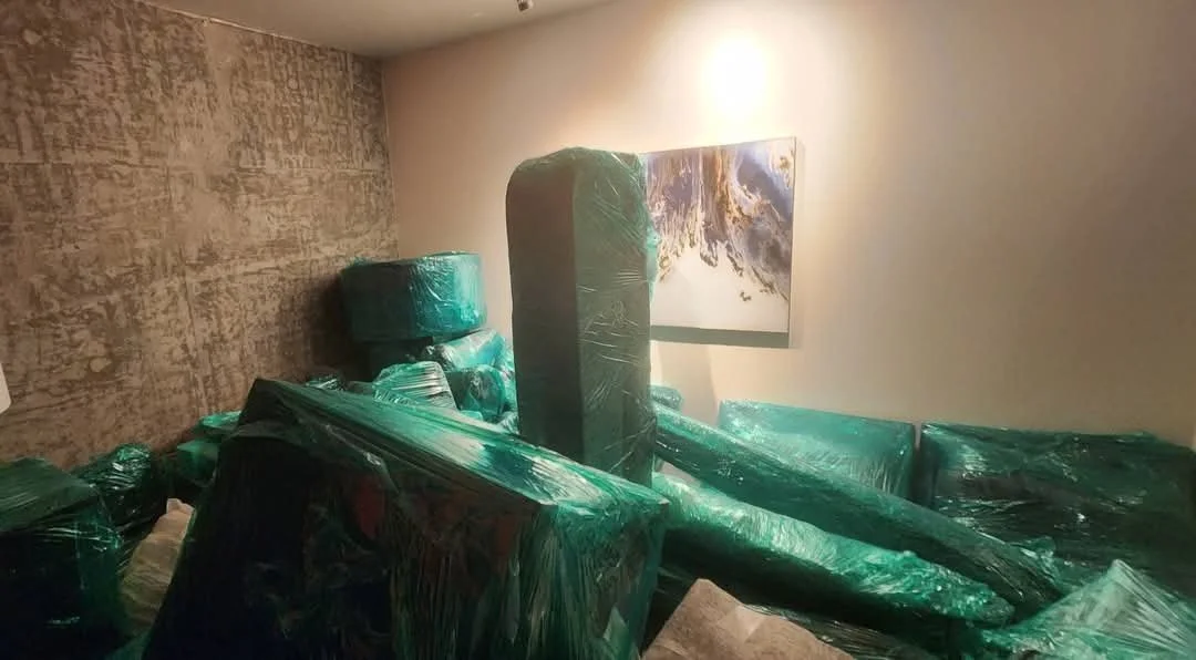 Room filled with green plastic-wrapped furniture and items, with a framed picture hanging on the wall.