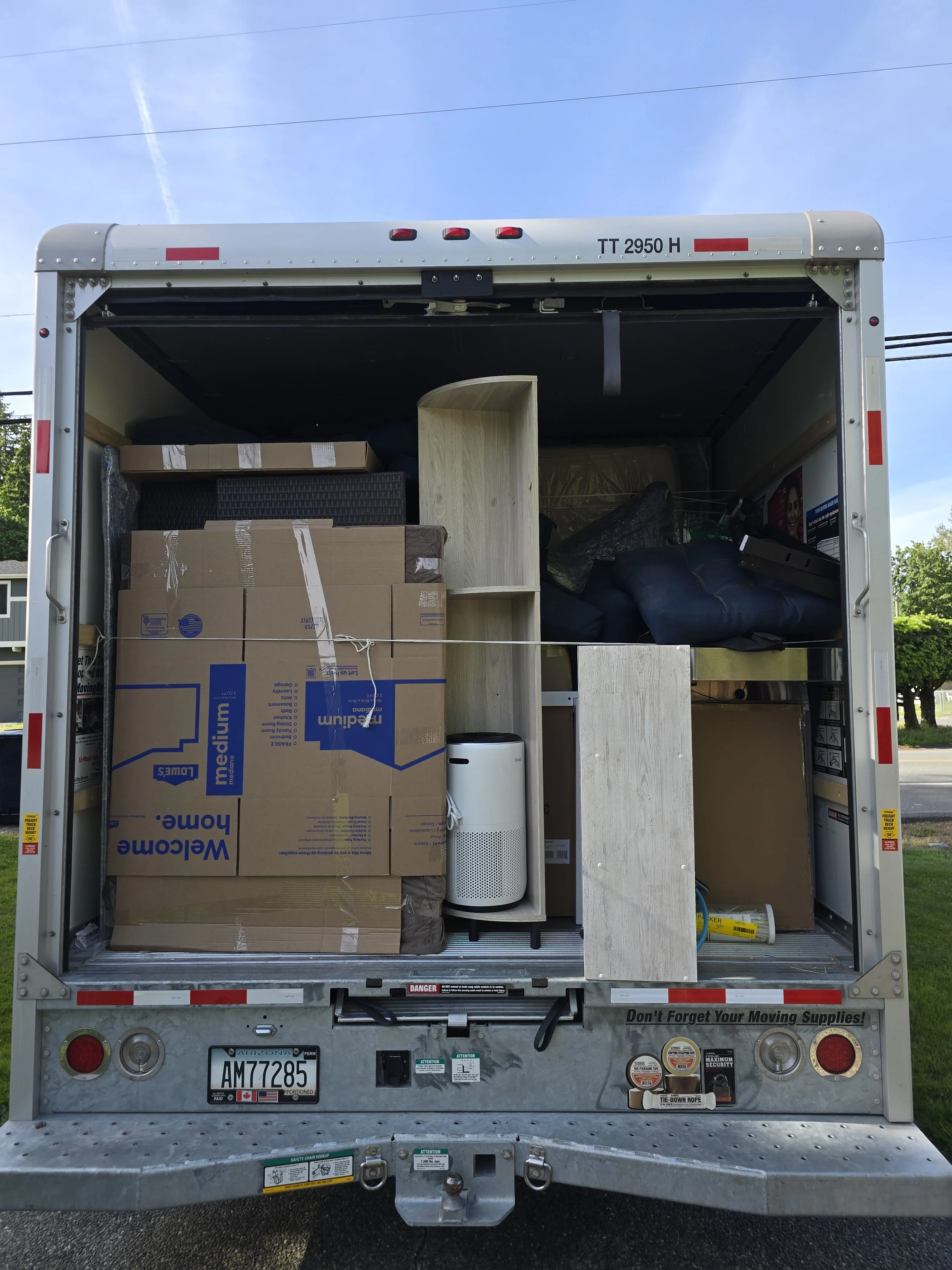 Open moving truck packed with boxes, furniture, and household items, including a white air purifier.