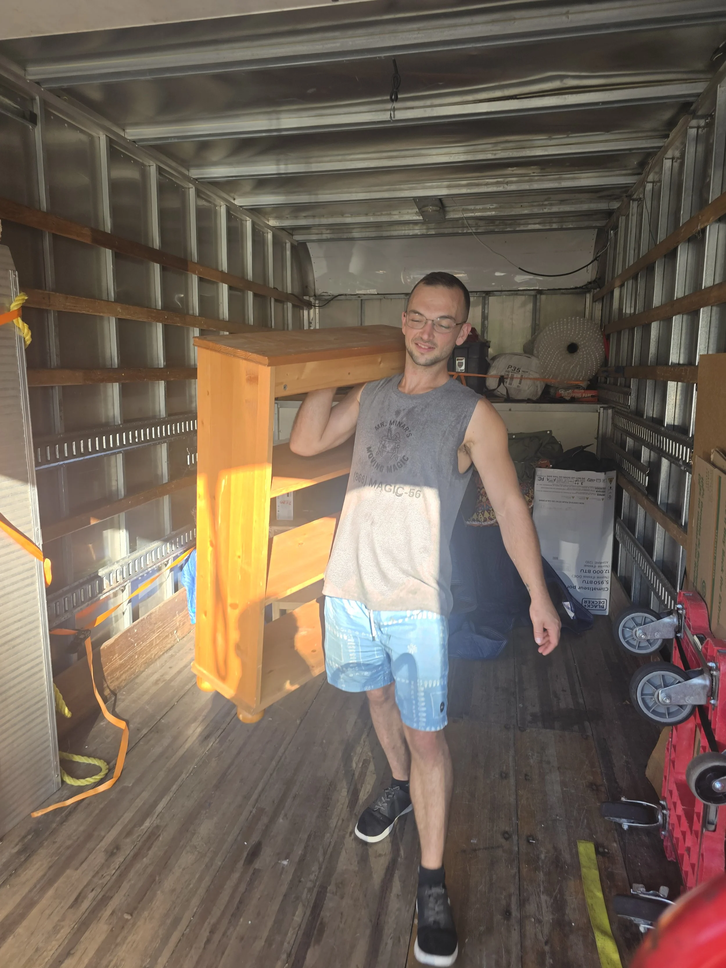 Man carrying a wooden table inside a storage truck or moving van.