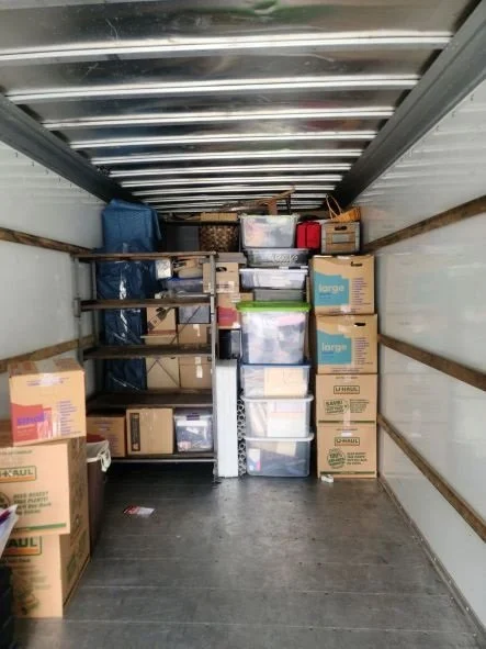 Inside of a moving truck loaded with cardboard boxes and plastic storage bins stacked along the walls and on top of each other.