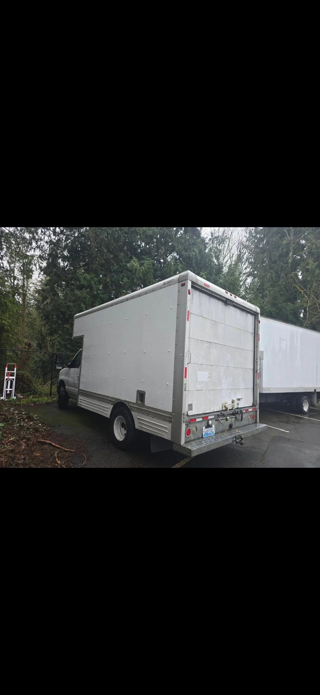 A white box truck parked in a lot with trees in the background.