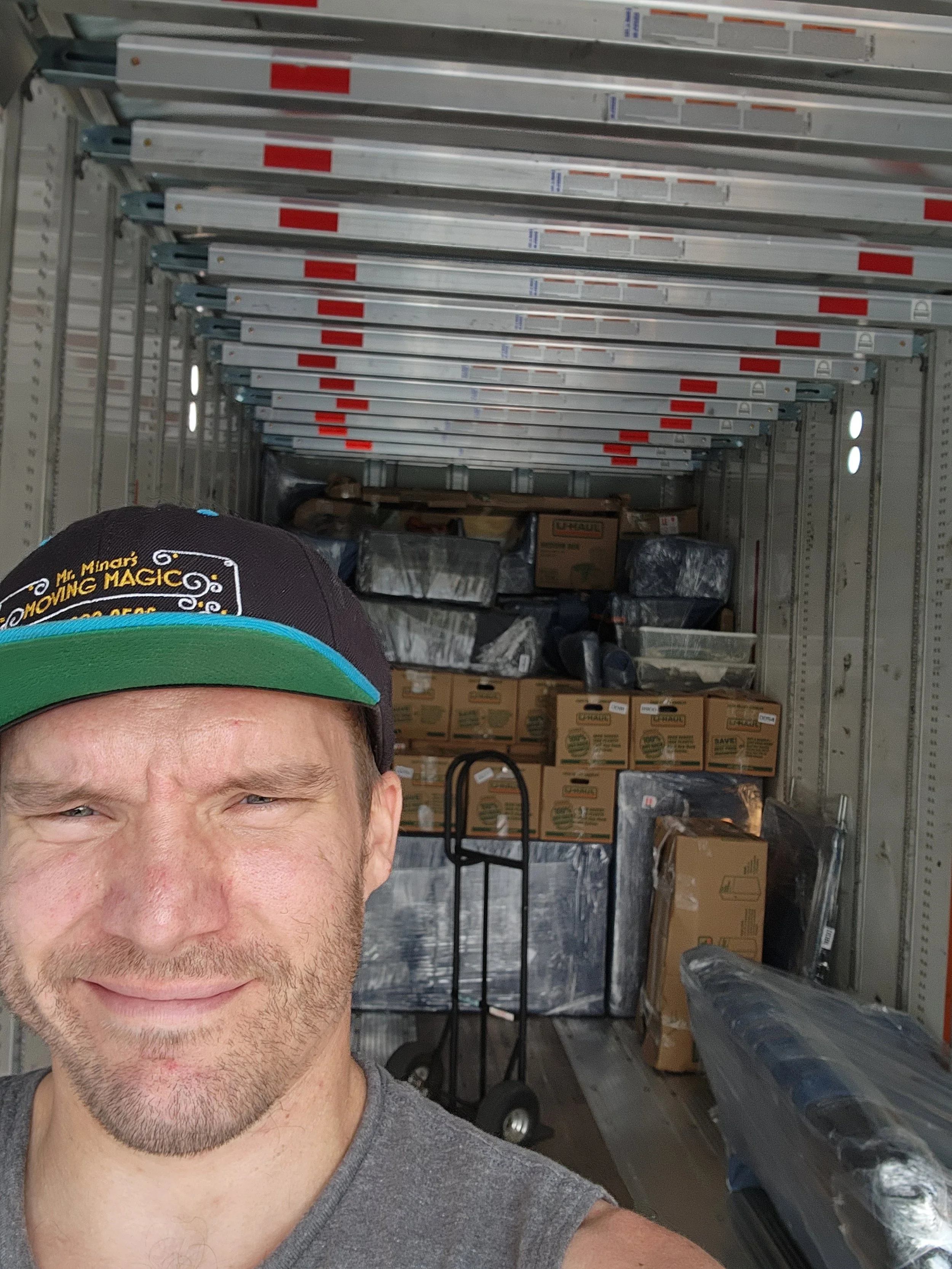 Man taking a selfie inside a moving truck with boxes and equipment in the background.