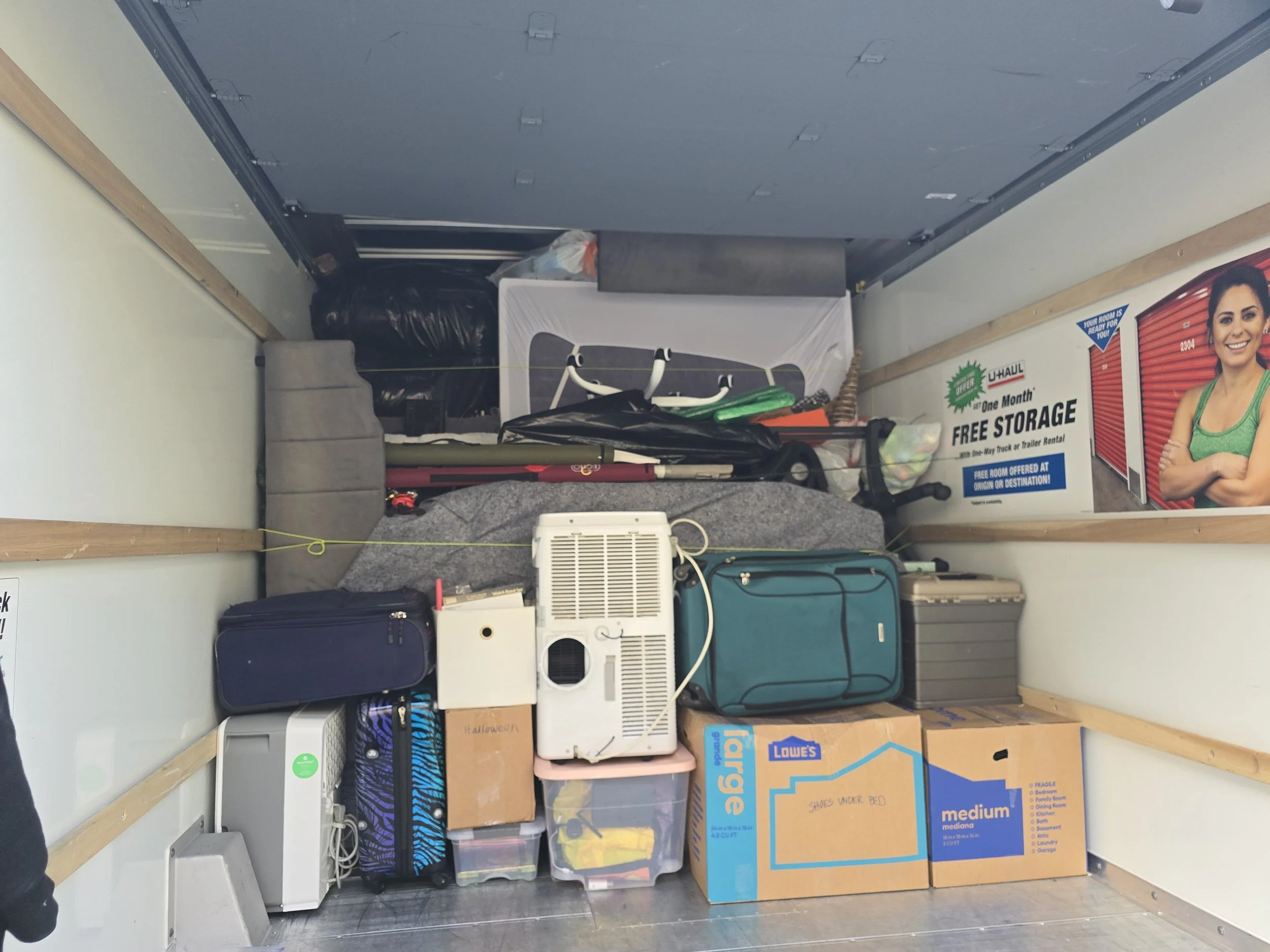 Packed moving truck filled with boxes, suitcases, household items, and a U-Haul promotional sign.