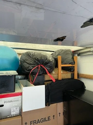 Storage space filled with various bags, a cardboard box labeled 'Fragile,' and other miscellaneous items.