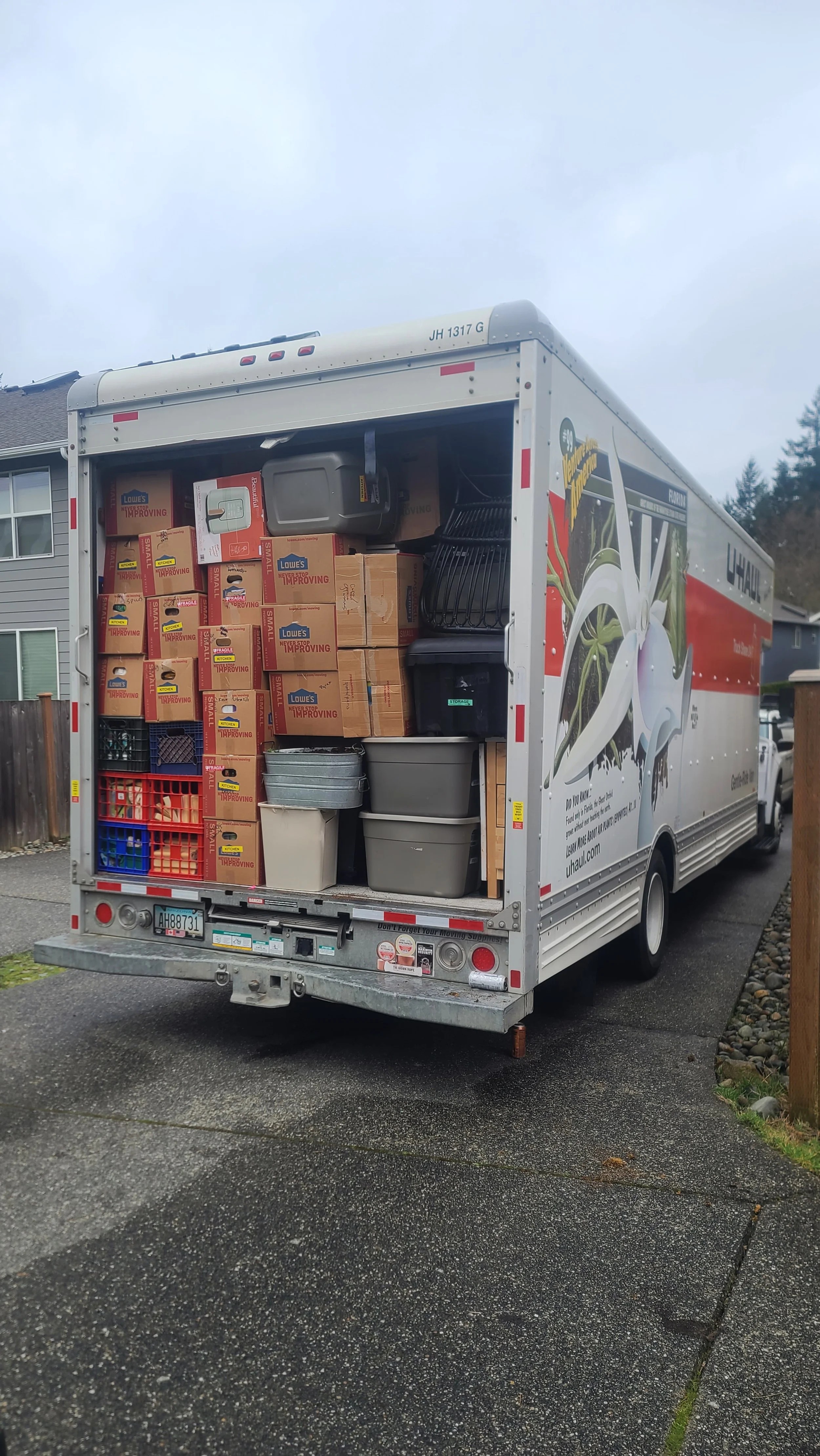 U-Haul moving truck with its rear door open, filled with boxes, plastic storage bins, and crates.