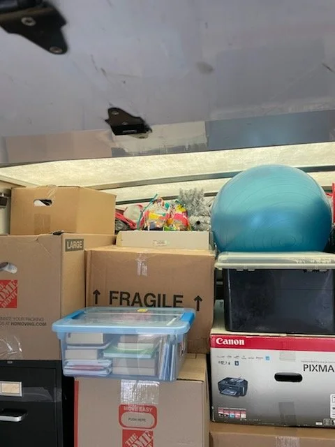 A pile of cardboard boxes, some labeled 'large' and 'fragile', along with a clear plastic container, a blue exercise ball, and a Canon Pixma printer box stacked on top of boxes.