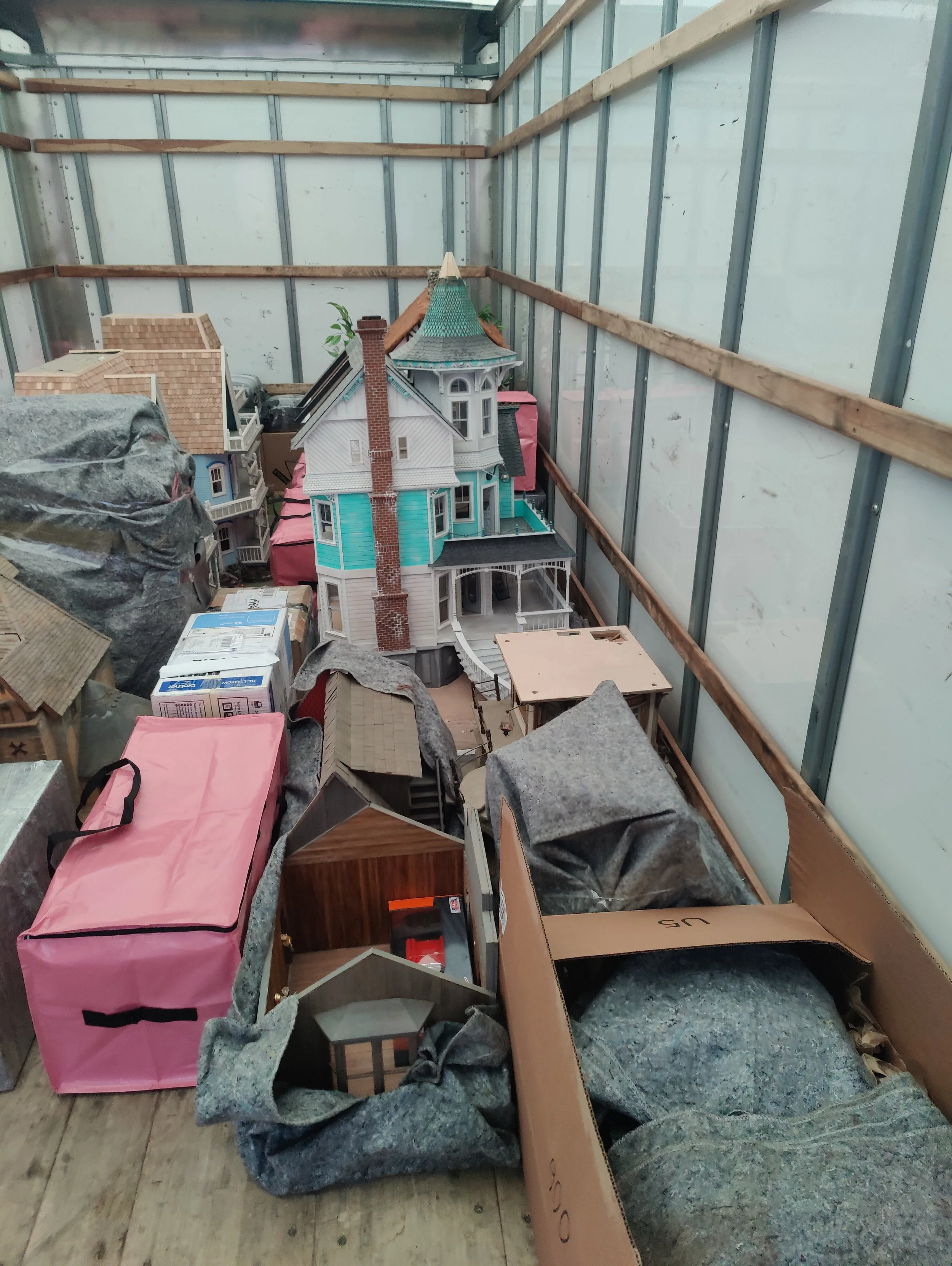 Collection of dollhouses in a storage container with packing material and boxes around them.