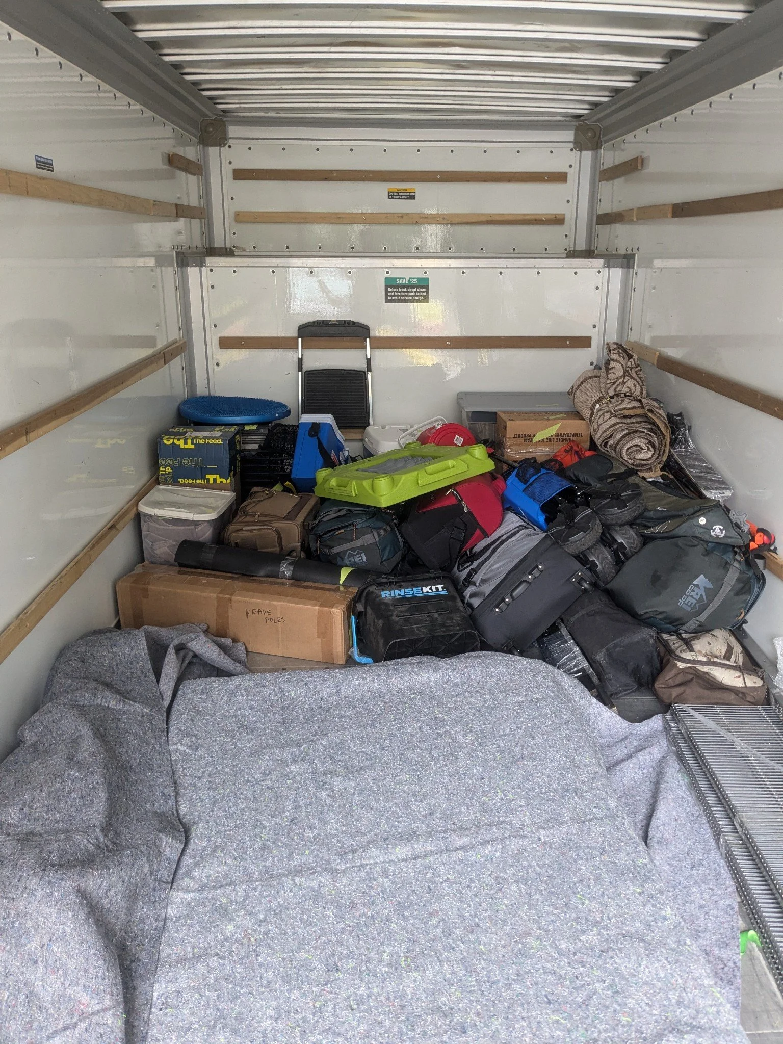 Empty truck storage with various packed bags, a rolled-up blanket, and a cardboard box on the floor.