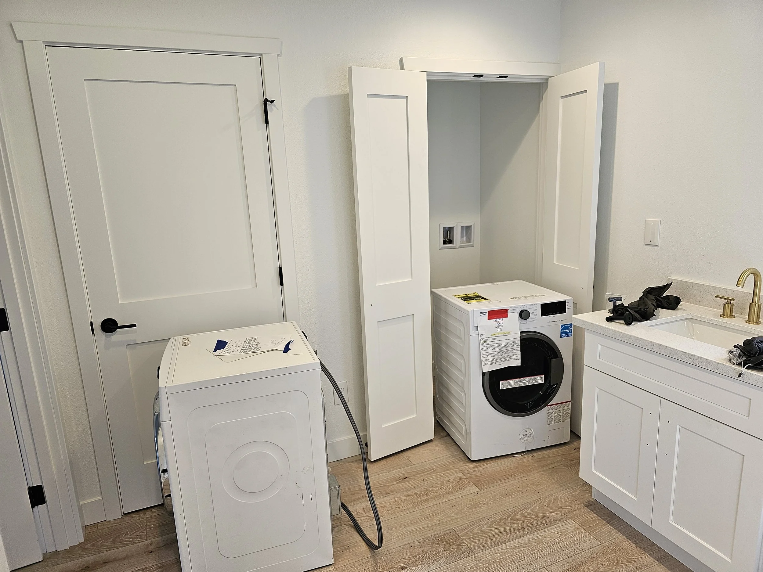 Laundry room with washer and dryer, white cabinets, a sink with gold faucet, and a door leading to another room.