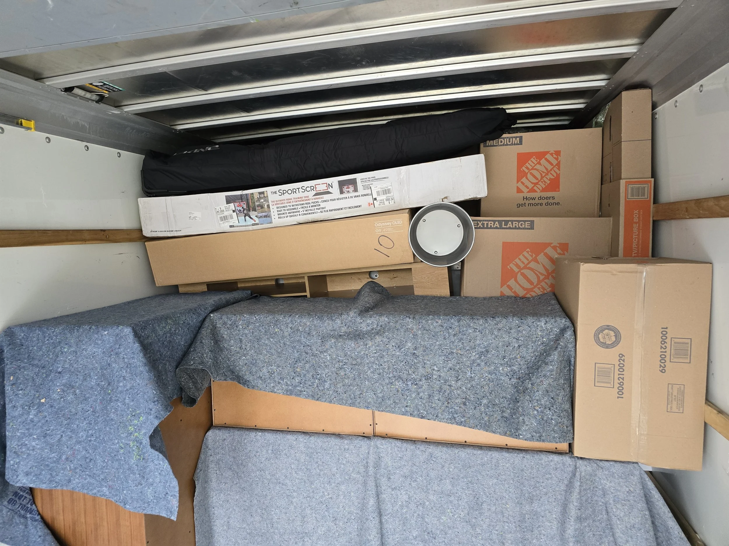 Empty storage unit with cardboard boxes, a rolled-up mat, a small table, and a black bag.