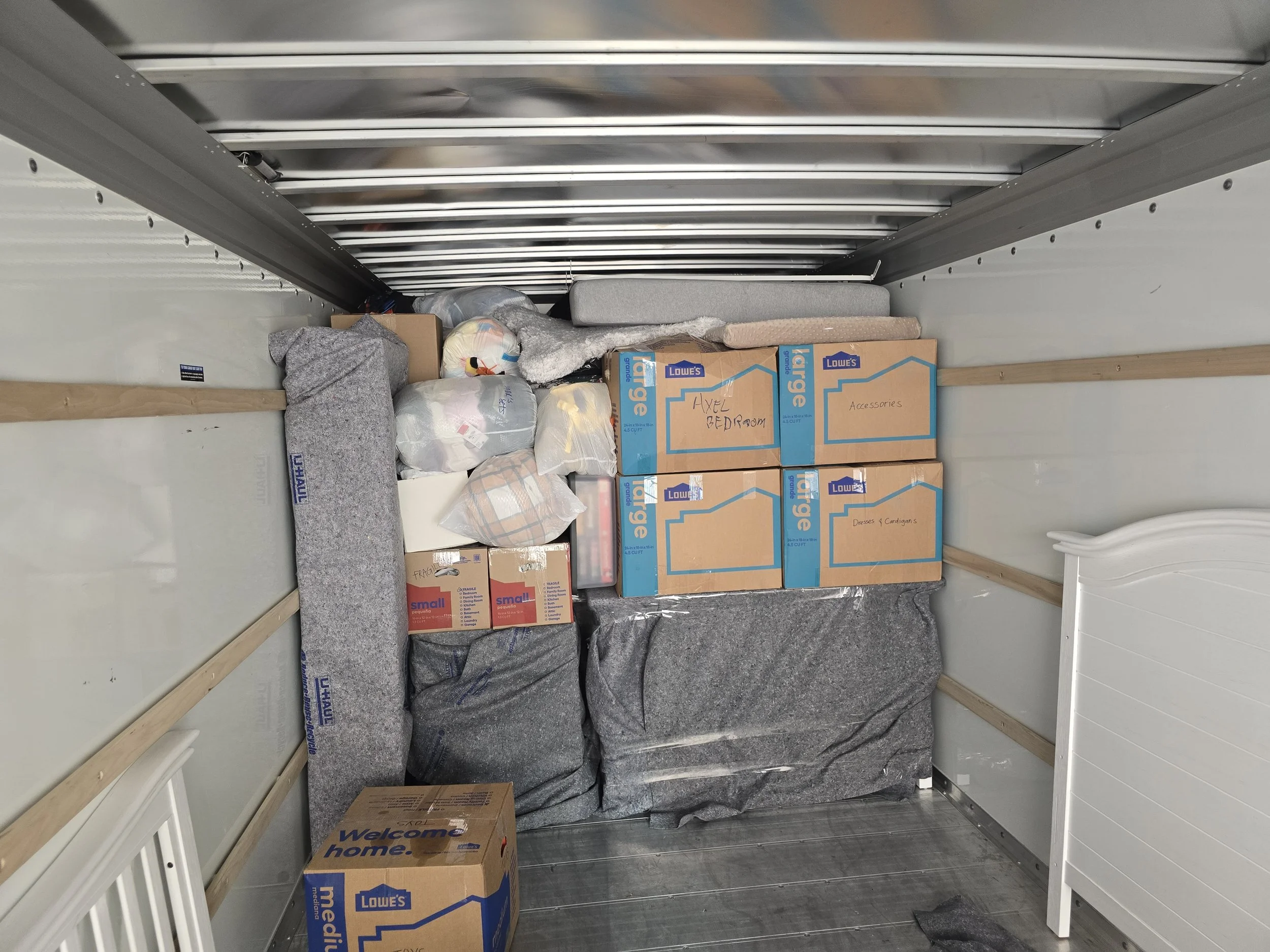 Interior of a moving truck filled with boxes, packed bedding, and miscellaneous household items for moving.