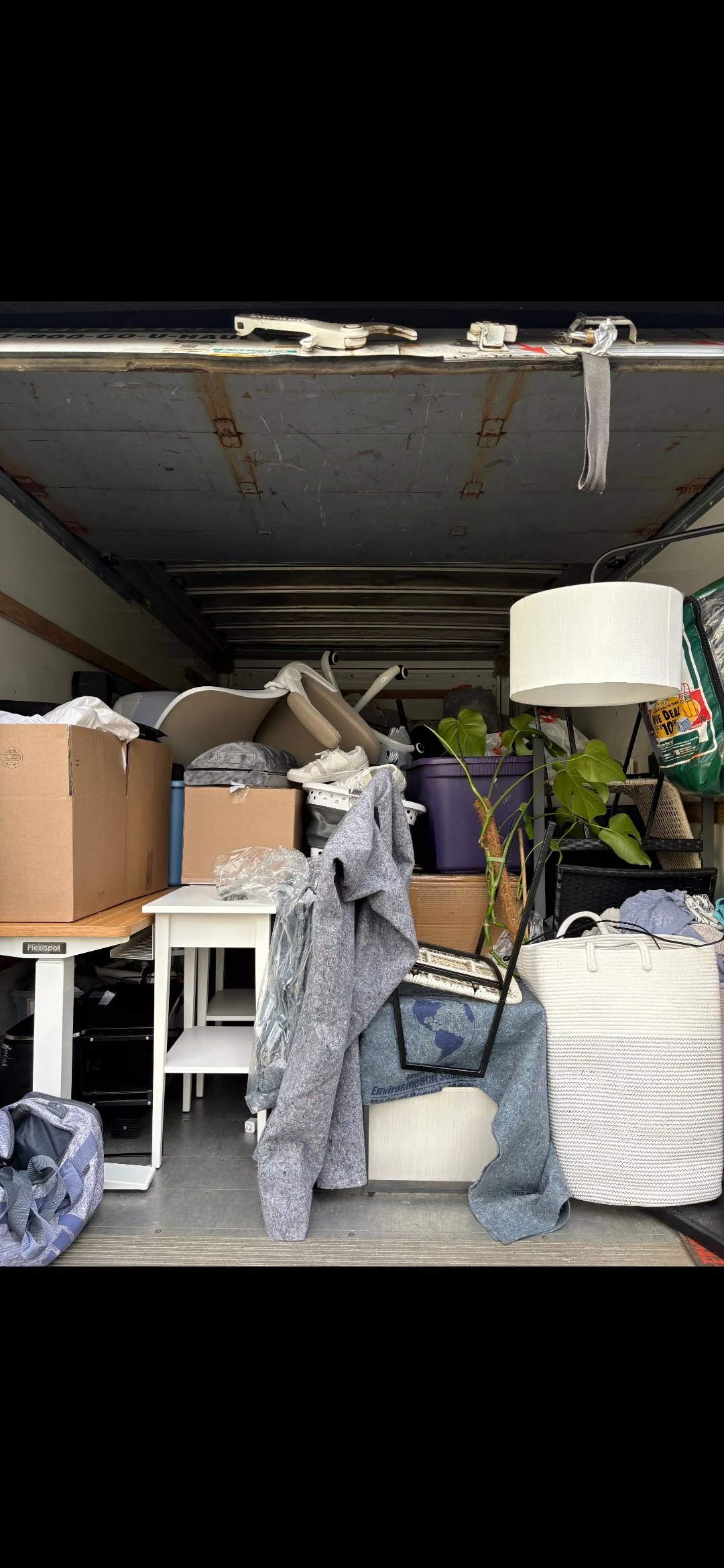 Miscellaneous household items in a cluttered truck or storage unit, including furniture, boxes, a plant, and a lamp.