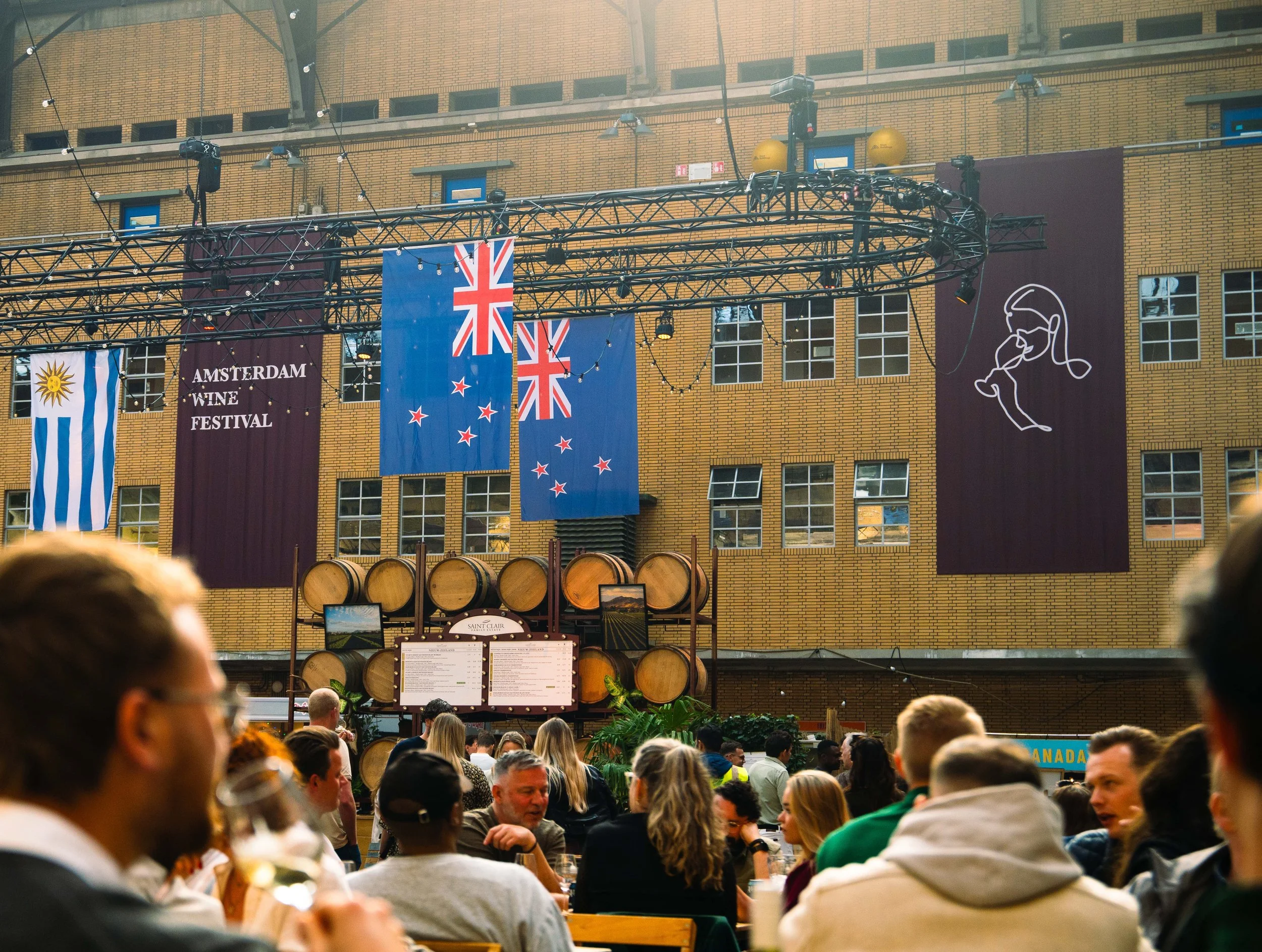 Bezoekers op het Amsterdam Wine Festival met vlaggen, wijnbar en levendige sfeer.