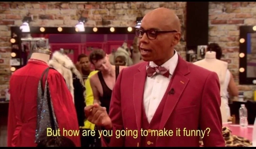 Photo of RuPaul in a reddish suit with a red plaid bowtie. The meme text at the bottom reads "But how are you going to make it funny?"