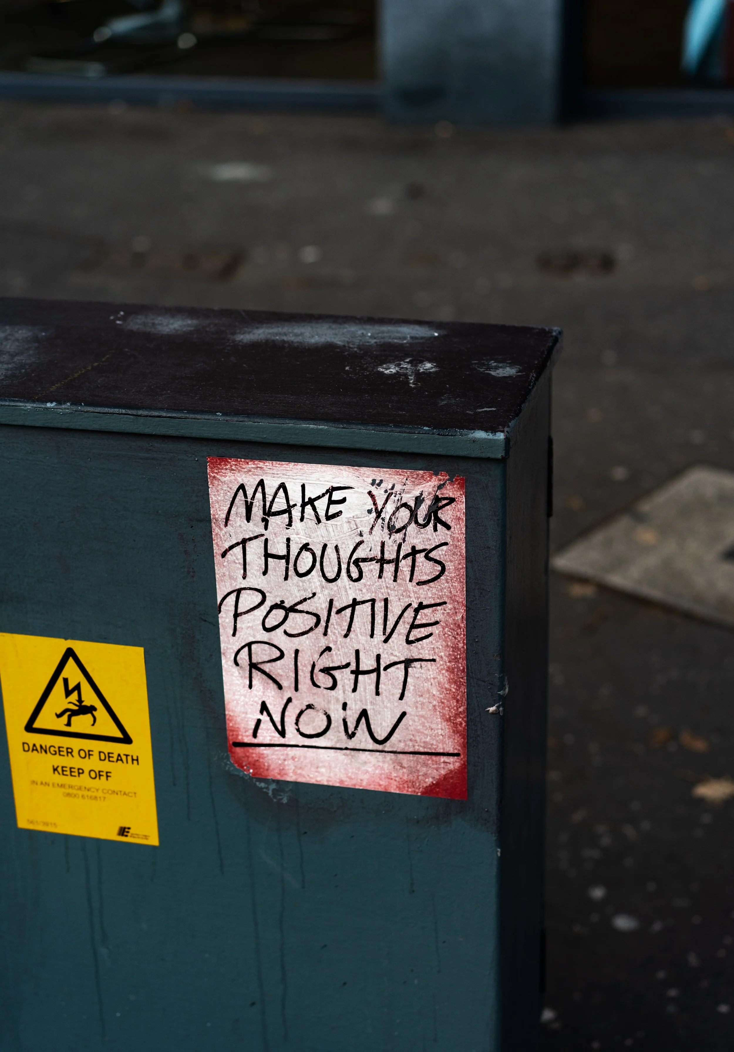 Sign with "MAKE YOUR THOUGHTS POSITIVE RIGHT NOW" on a box with a "Danger of Death" warning sign.