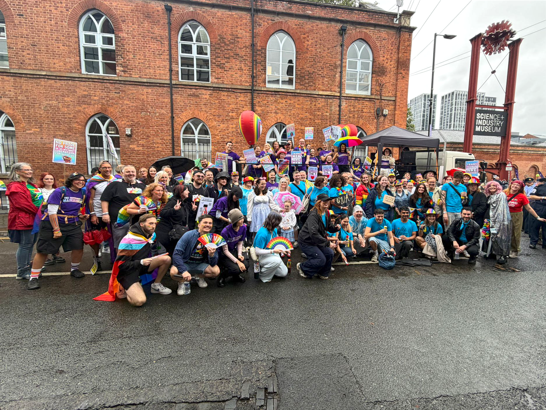 A large group from Greater Manchester’s universities gathers in colourful Pride clothing and waving rainbow flags at the Manchester Pride Parade outside the Science and Industry Museum.