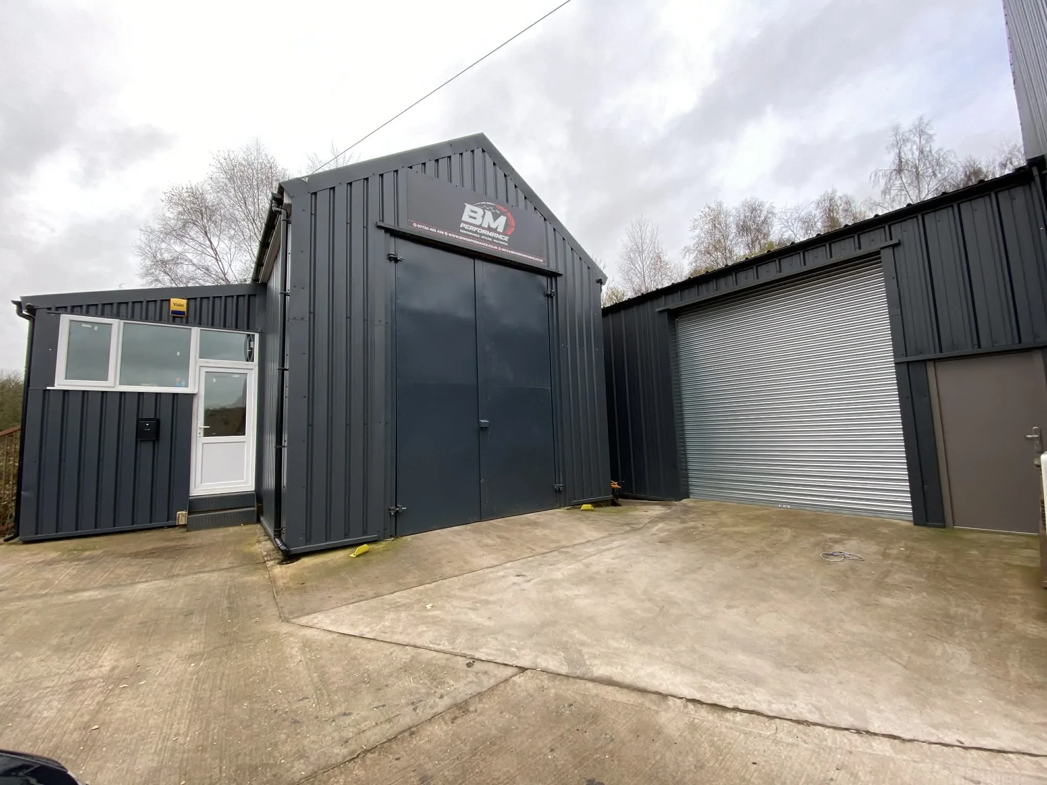 Industrial building with a large blue rolling shutter door, a smaller grey door, and a white door with a window and mail slot, set on a concrete driveway.