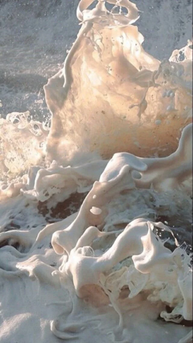 Close-up of foamy waves crashing on the shore, creating swirling white patterns in the water.