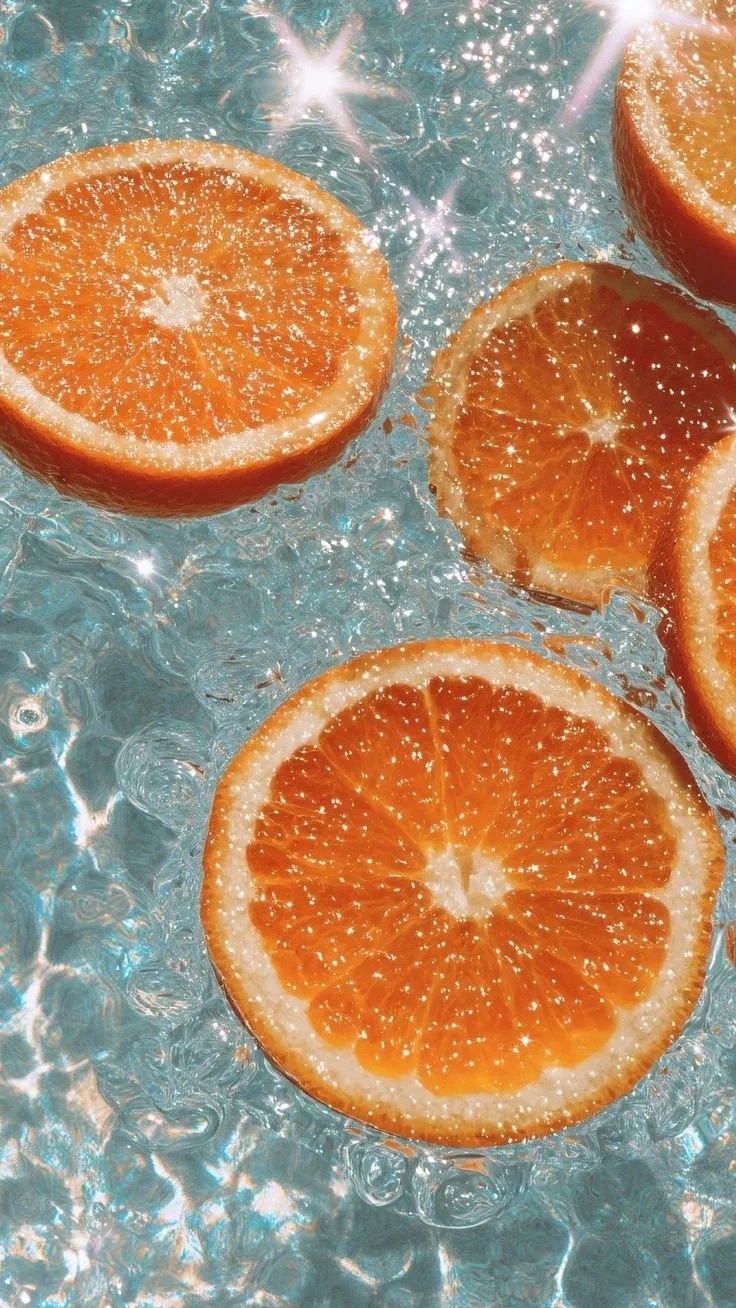 Several orange slices floating on water with sunlight reflecting off the surface.