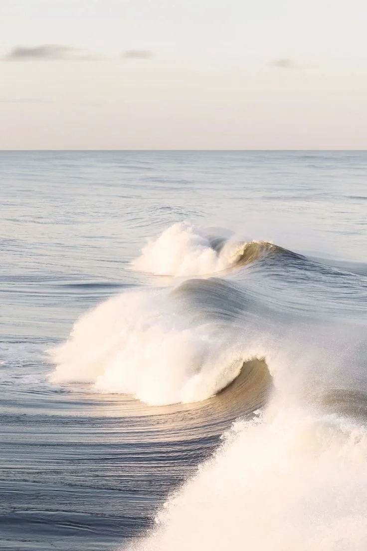 Waves crashing in the ocean during daytime with a cloudy sky.