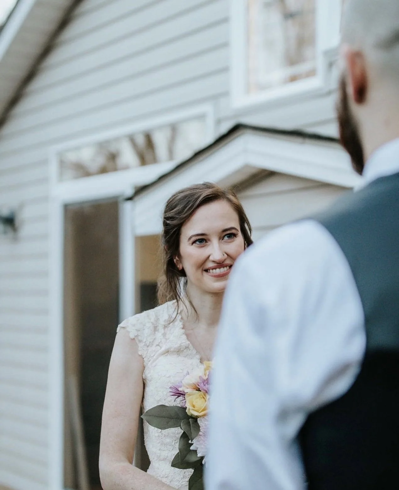 A woman in a wedding dress smiling at a man during a wedding or special event.