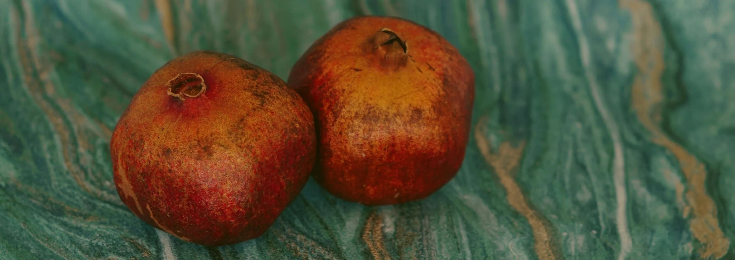 Twee rijpe granaatappels op een gemarmerde groene achtergrond.