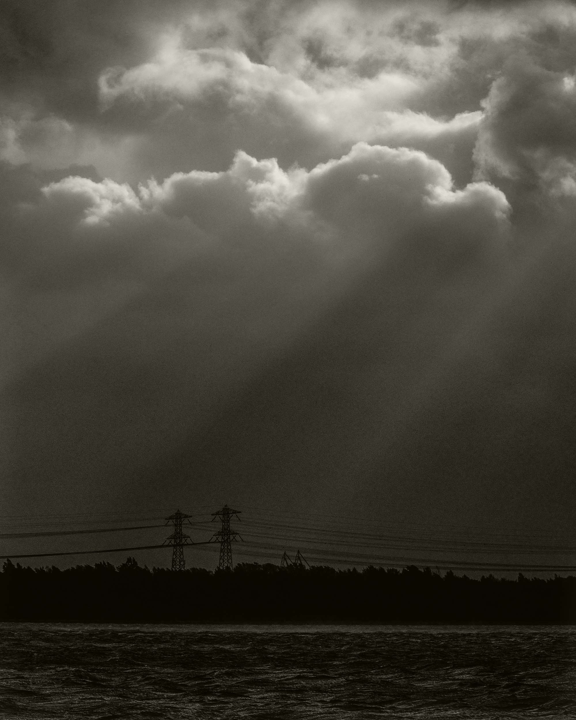 Donkere wolken boven een wateroppervlak en hoogspanningsmasten op de achtergrond.