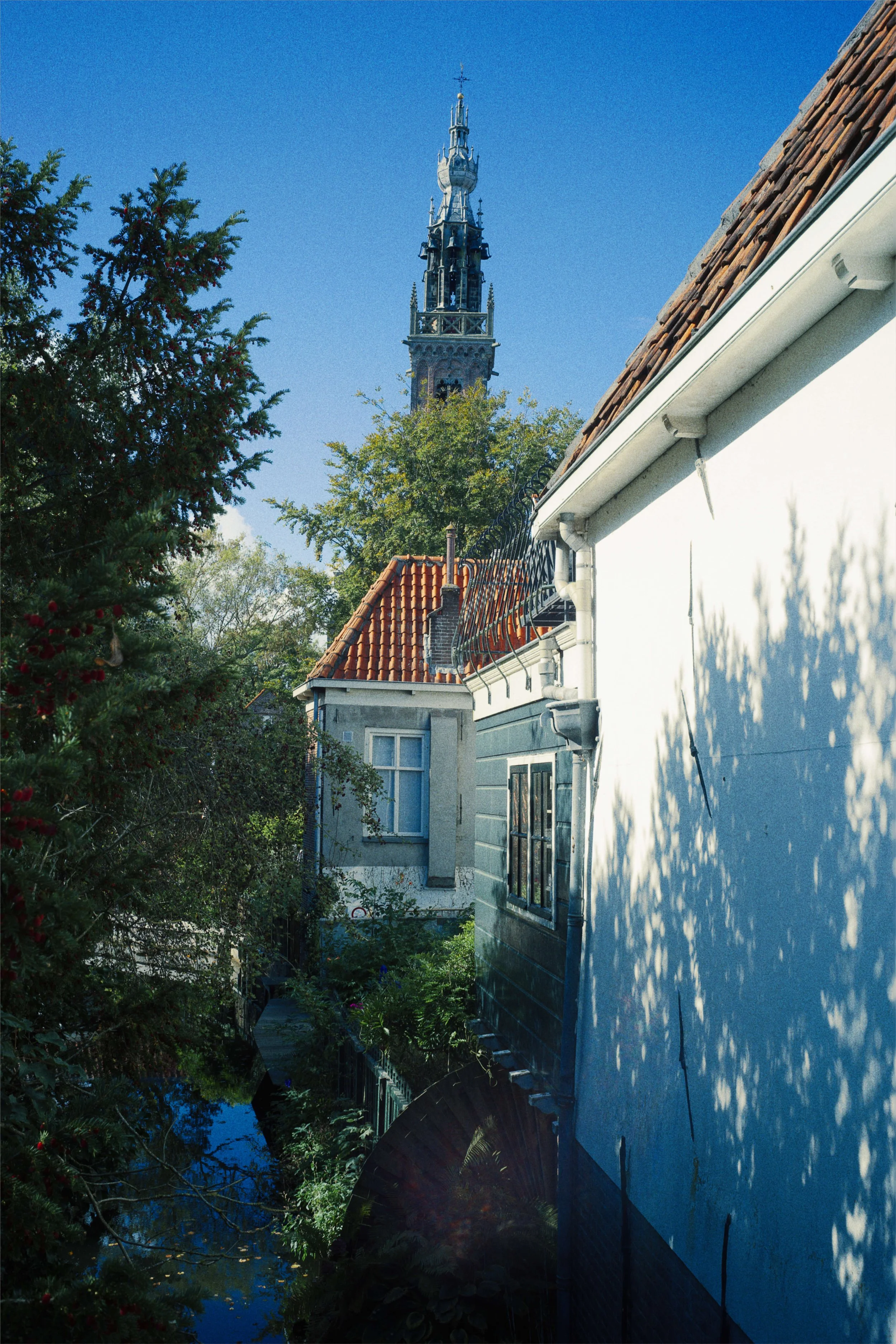 Een foto van een smal plein met een watergezicht, omgeven door huizen met rode en blauwe daken, met een toren op de achtergrond onder een blauwe hemel.