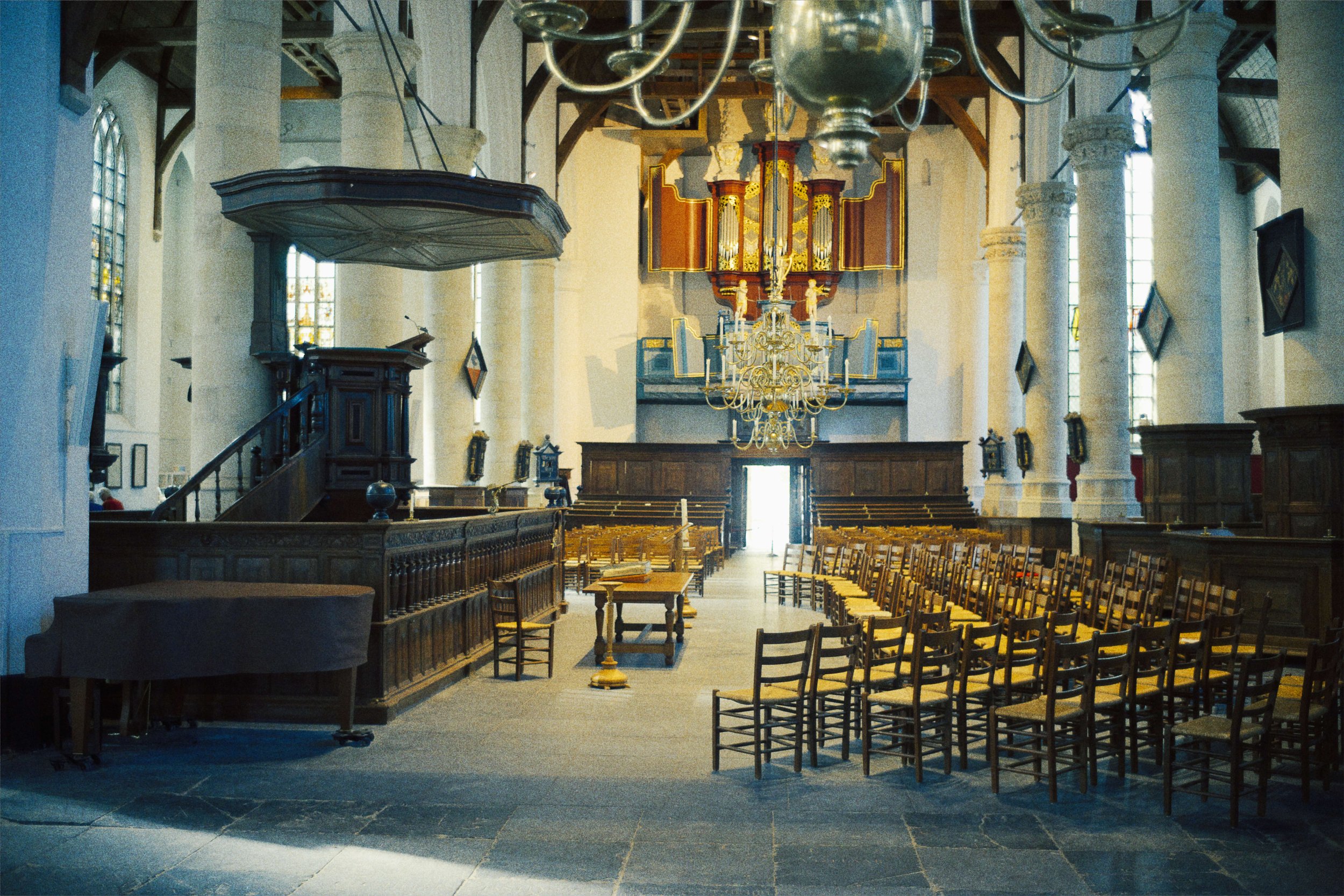 Interieur van een historische kerk met houten banken, een orgel, kroonluchters en hoge kerktorentjes met glas-in-loodramen.