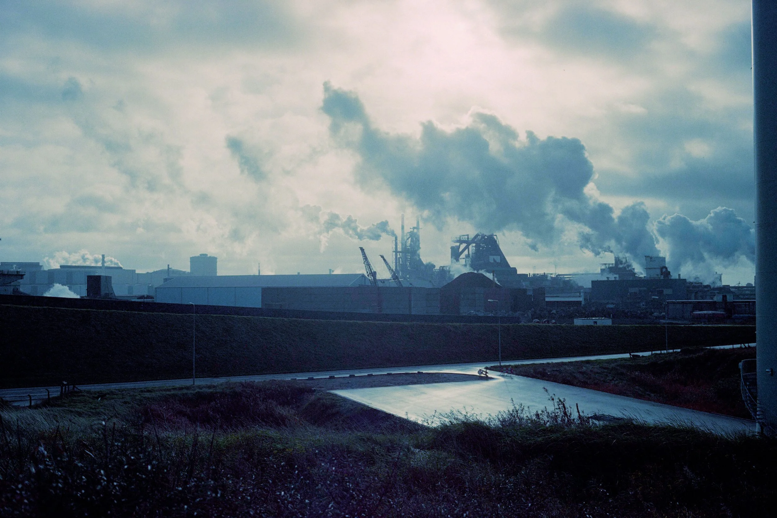 Industriecomplex met rook die uit schoorstenen opstijgt, onder bewolkte hemel.