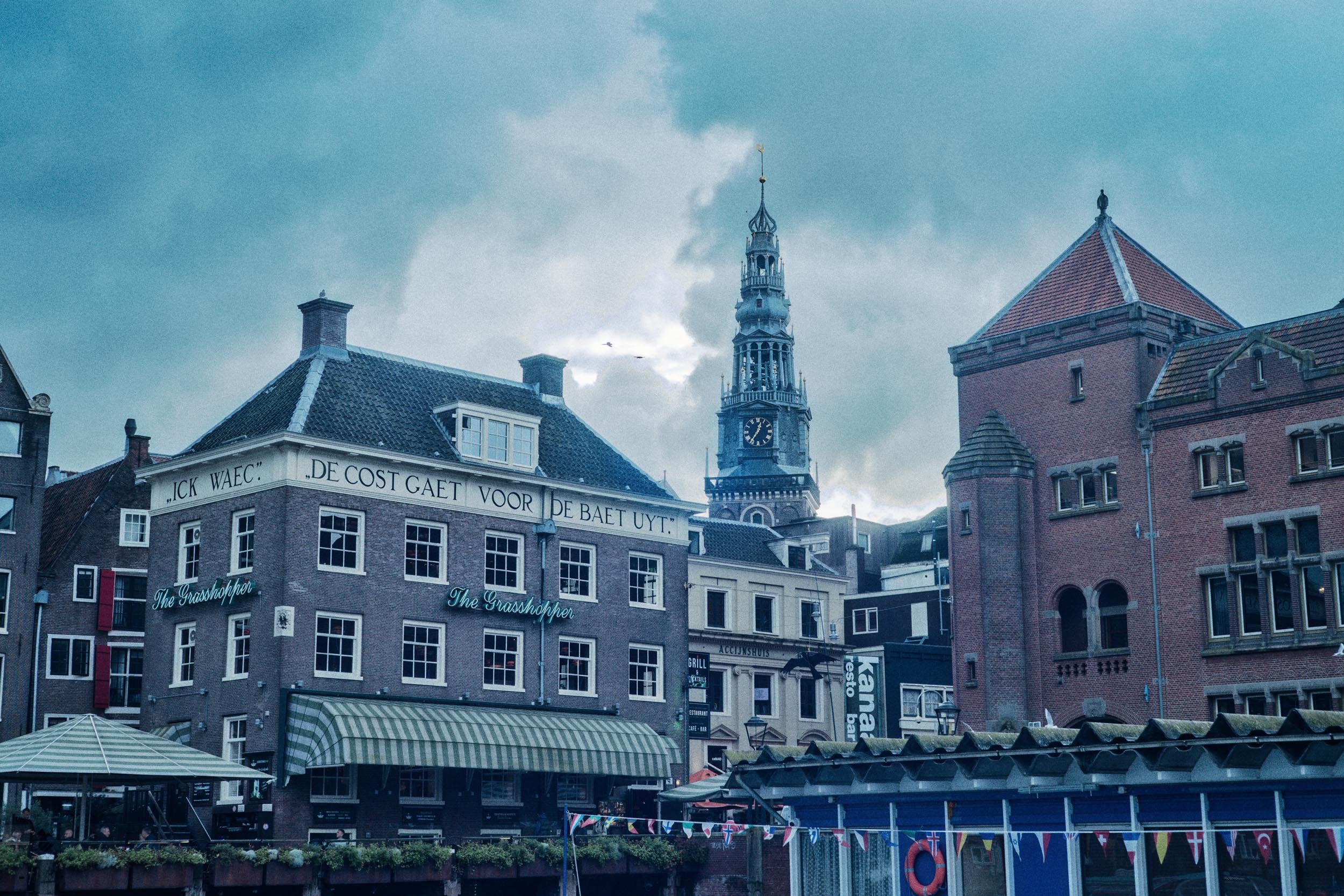 Een stadsgezicht met historische gebouwen en een kerktoren op de achtergrond, onder een bewolkte hemel.