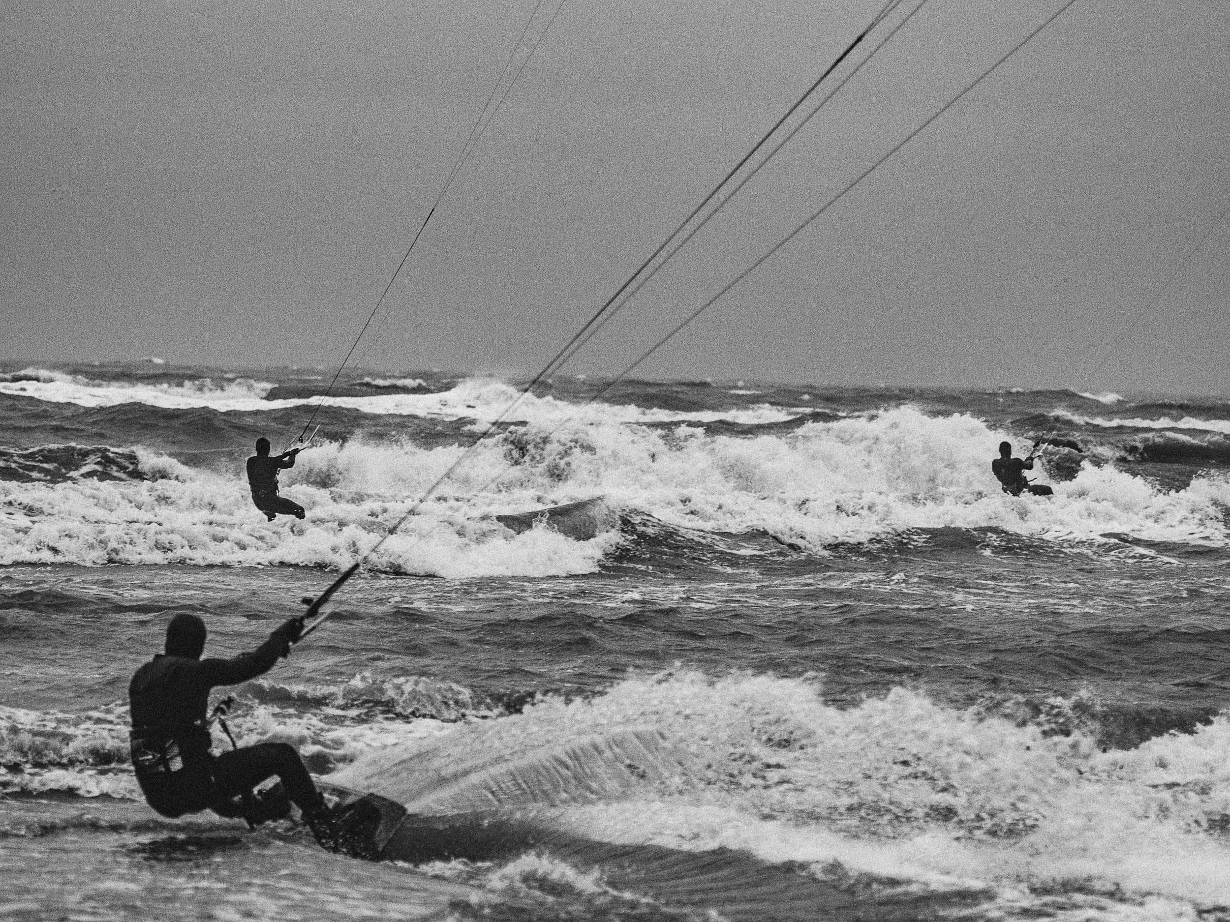 Twee mensen kite surfen op de oceaan met golven en een heldere lucht.