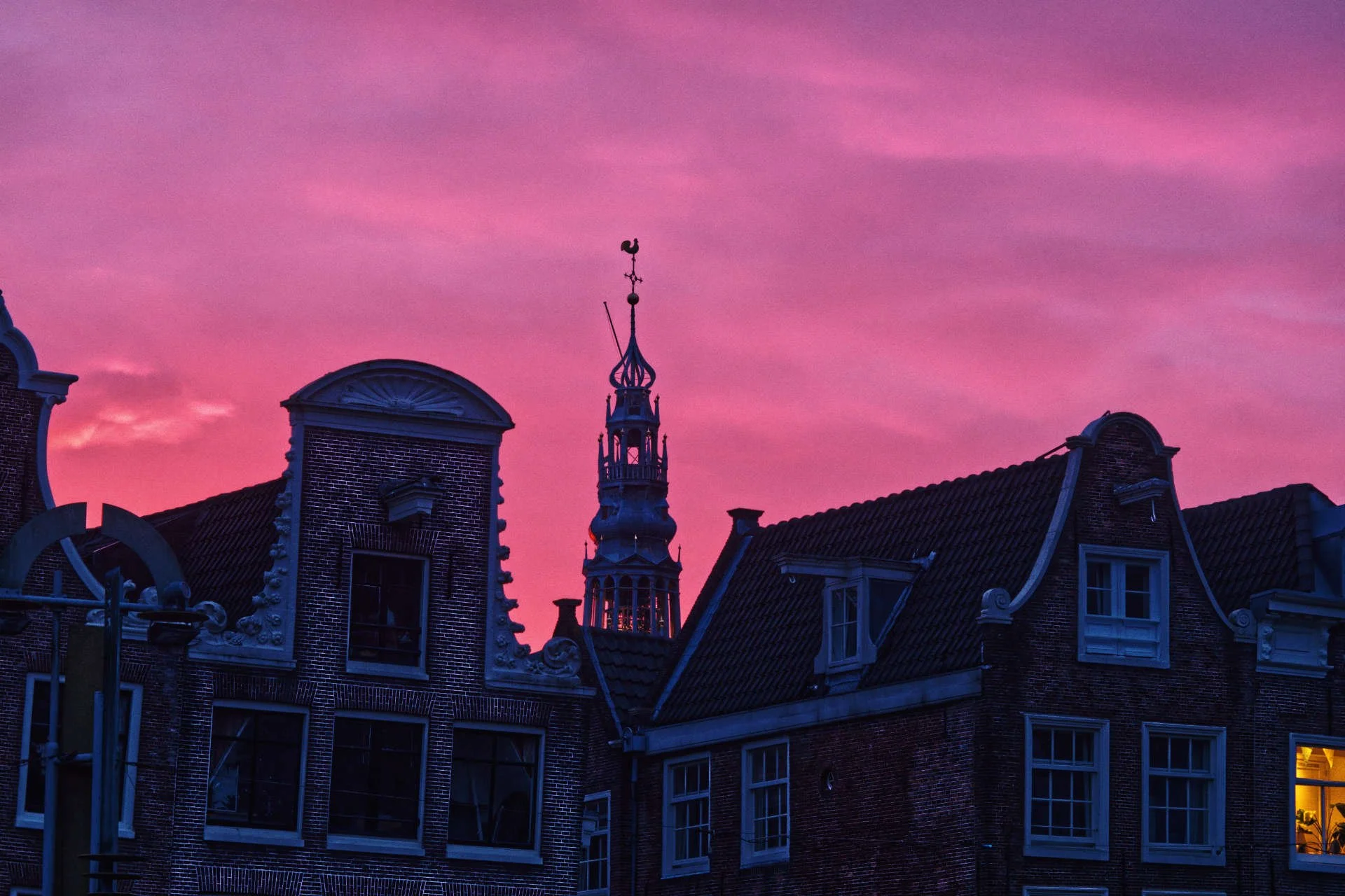 Uitzicht op historische Nederlandse gebouwen met een torentje op de achtergrond, onder een roze-paarse hemel tijdens zonsondergang.